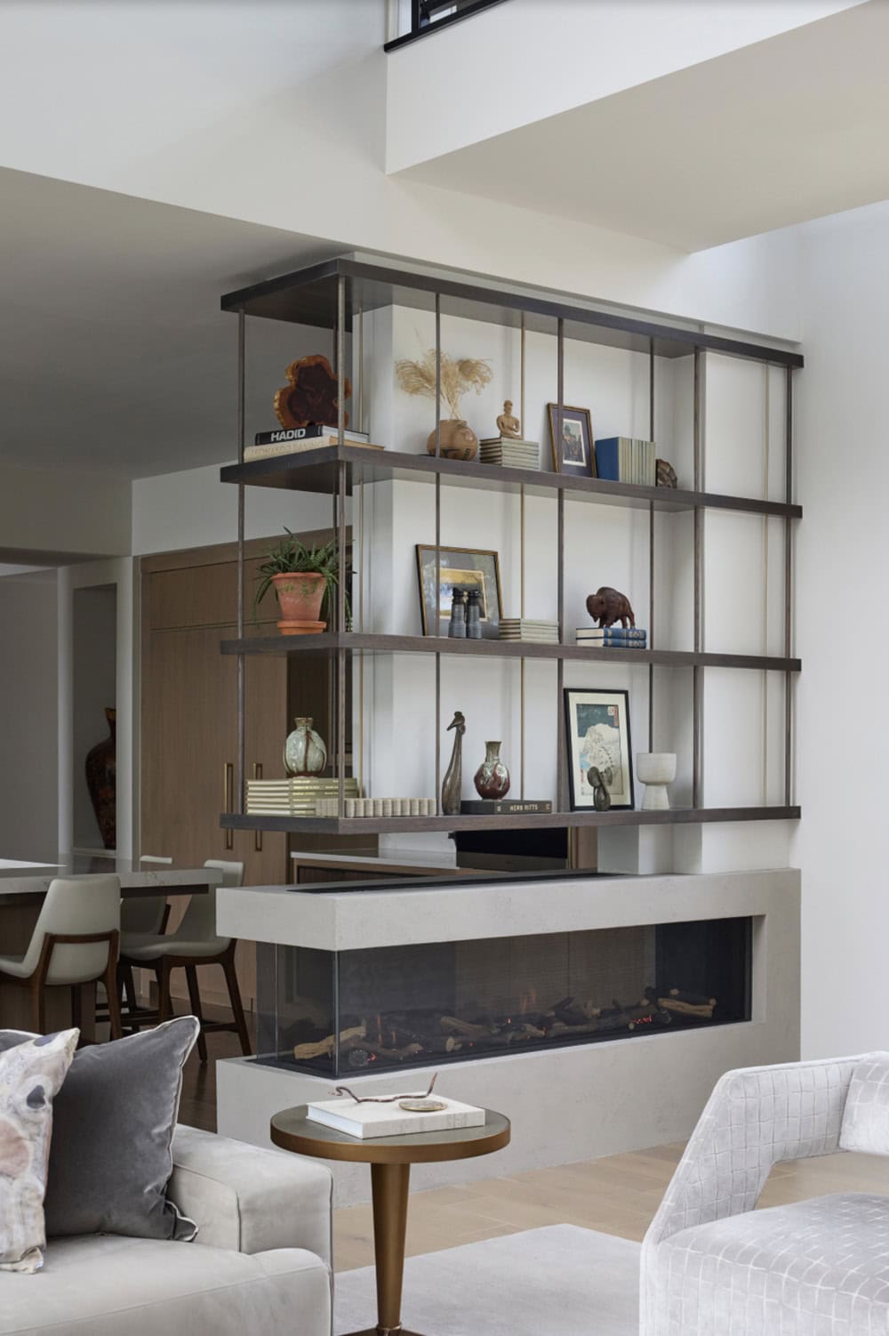 Metal-and-glass floating shelving unit displaying decor above a linear fireplace