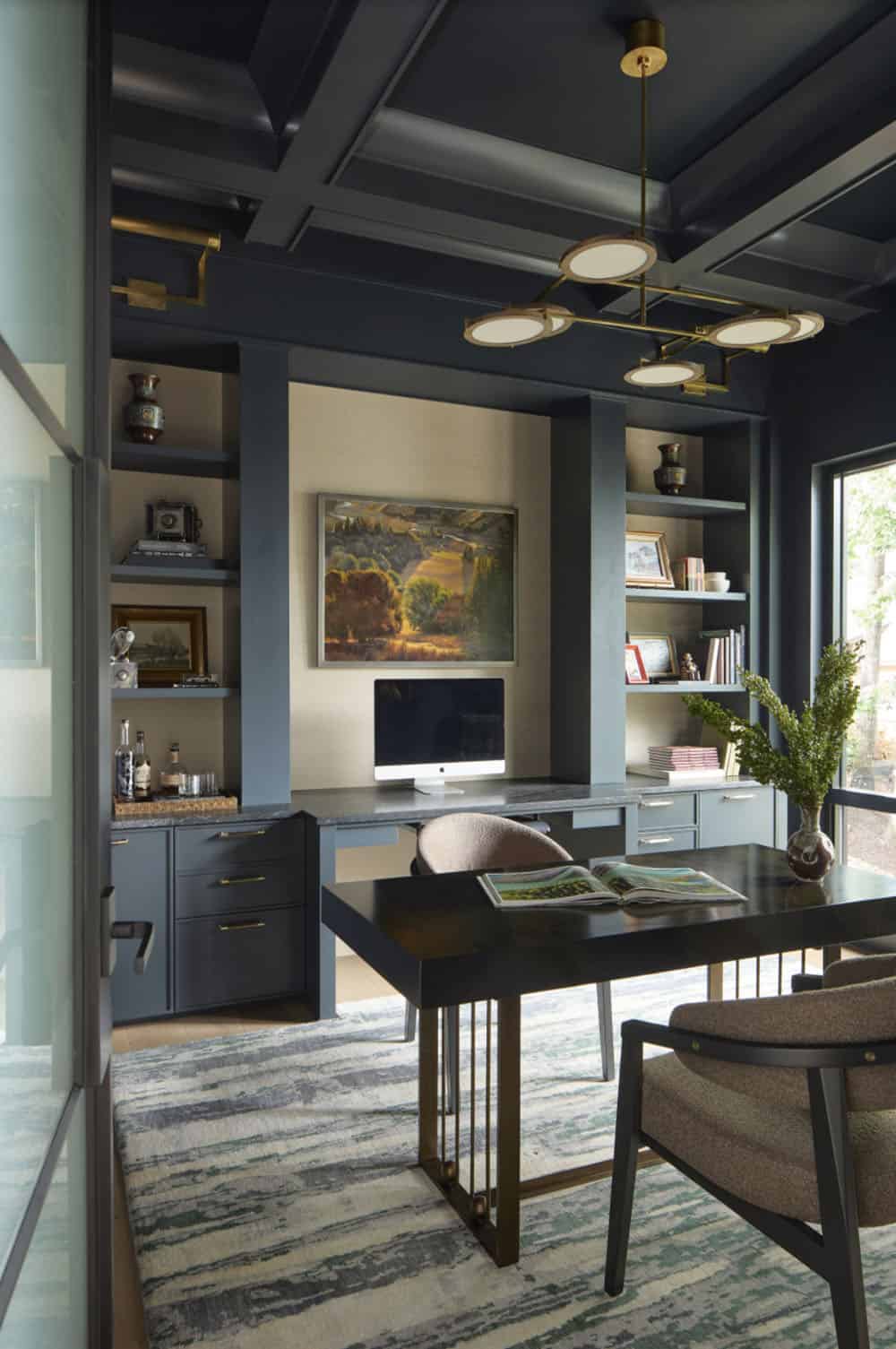 Dark blue home office with coffered ceiling, built-in shelving, brass fixtures, and a desk