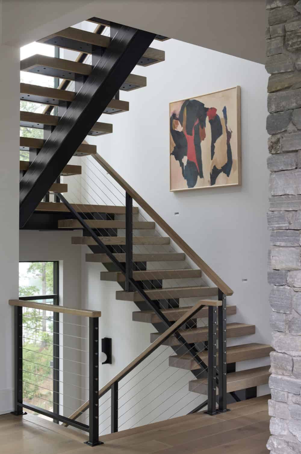 Floating staircase with black steel stringers, wood treads, and cable railing beside abstract artwork
