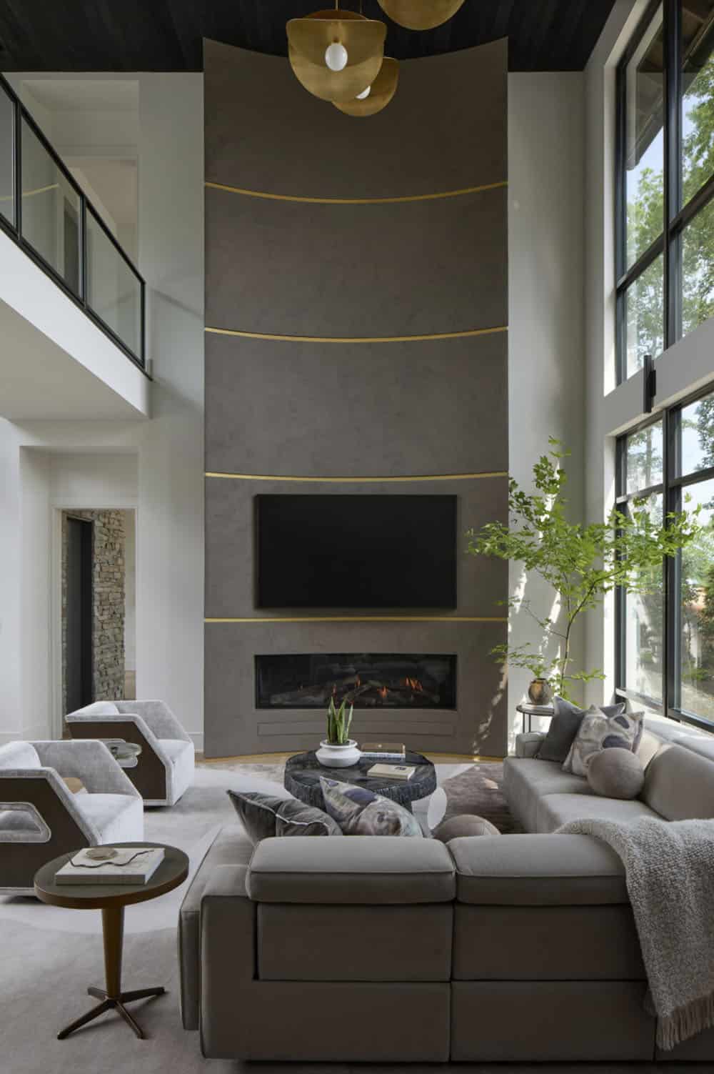 Two-story living room with a tall curved fireplace wall accented in brass and a sculptural pendant light