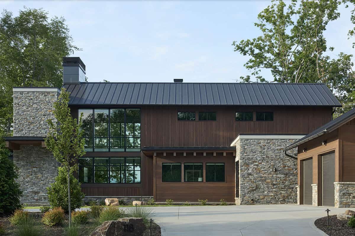 Front exterior of the house with stone chimney, dark metal roof, wood siding, and attached three-car garage