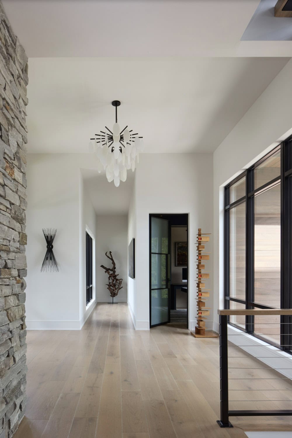 Bright entry hallway with sculptural pendant light, wall art, driftwood sculpture, and stone accent wall