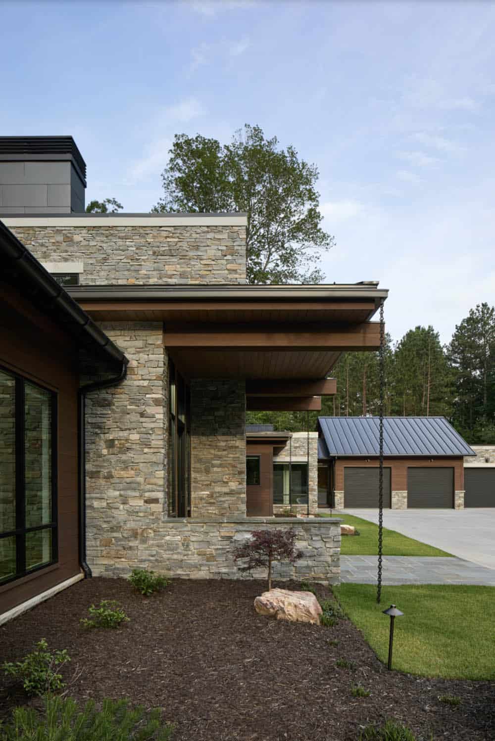 Side exterior view showing stacked stone walls, cantilevered roof overhang, and detached garage