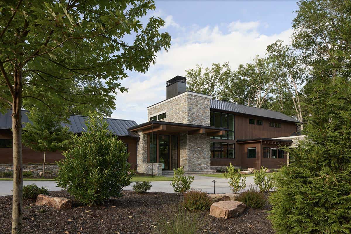 Front entrance tower with stone cladding, chimney, and covered wood entry porch among trees