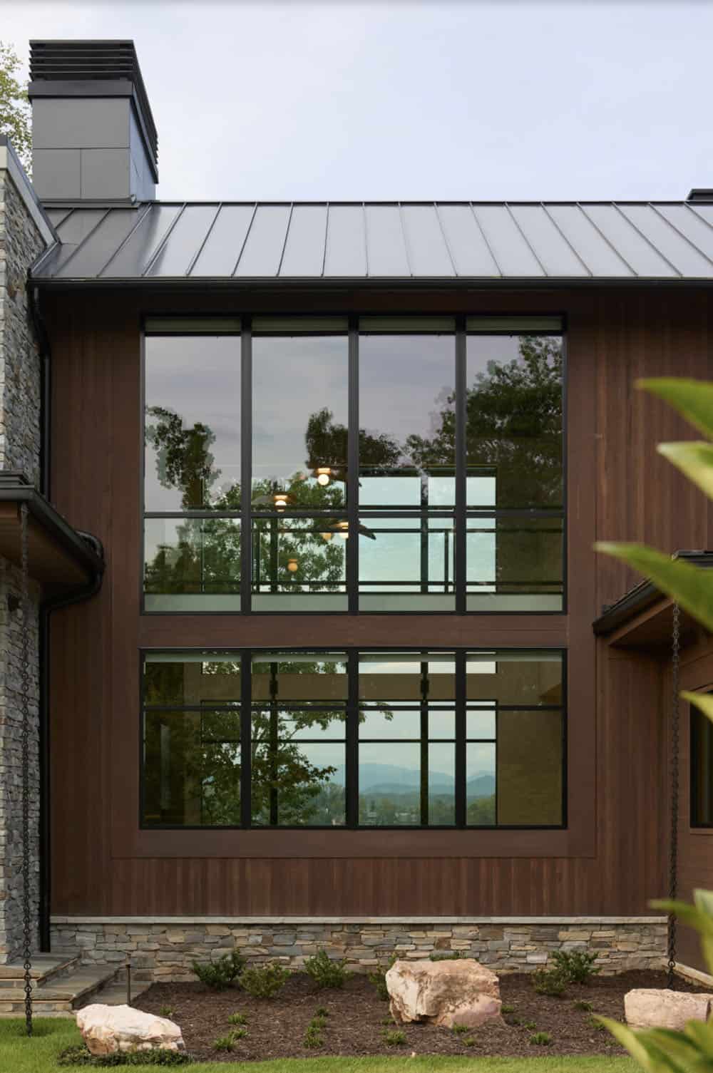 Close-up of two-story wood-framed windows reflecting trees and mountain views