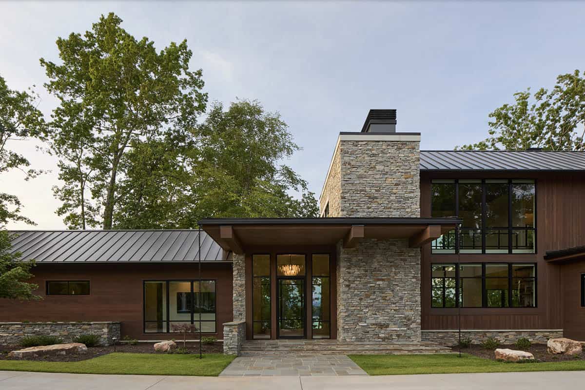 Front entrance with stacked stone chimney tower, glass doors, and chandelier visible inside