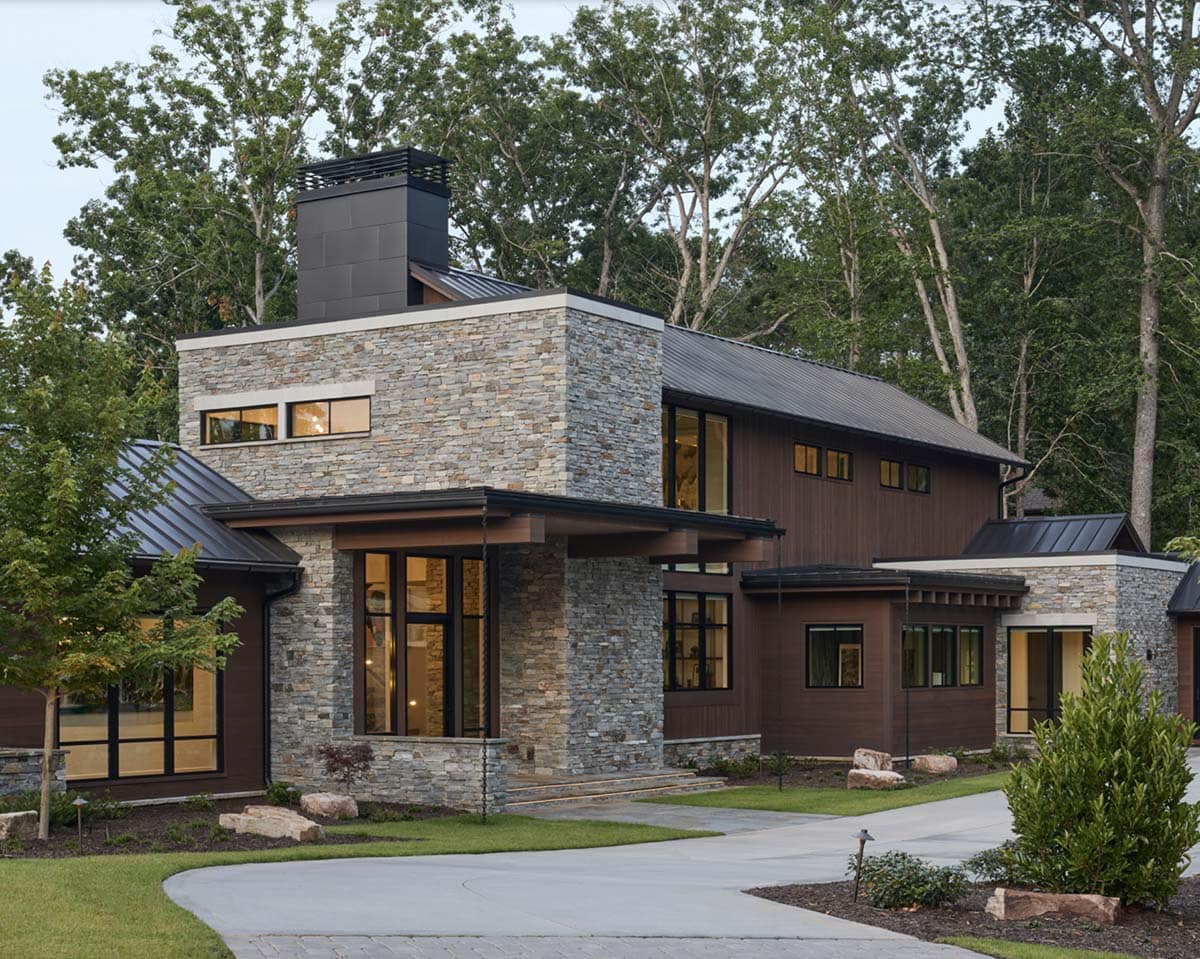 Dusk exterior view of the stone entry tower, dark wood siding, and metal roofline