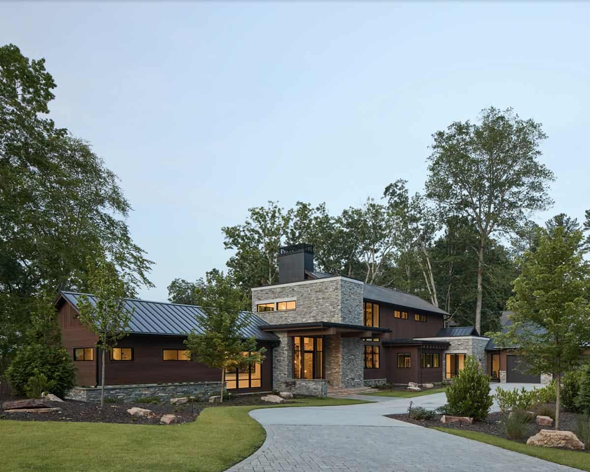 Wide dusk view of the house with illuminated windows and circular paver driveway