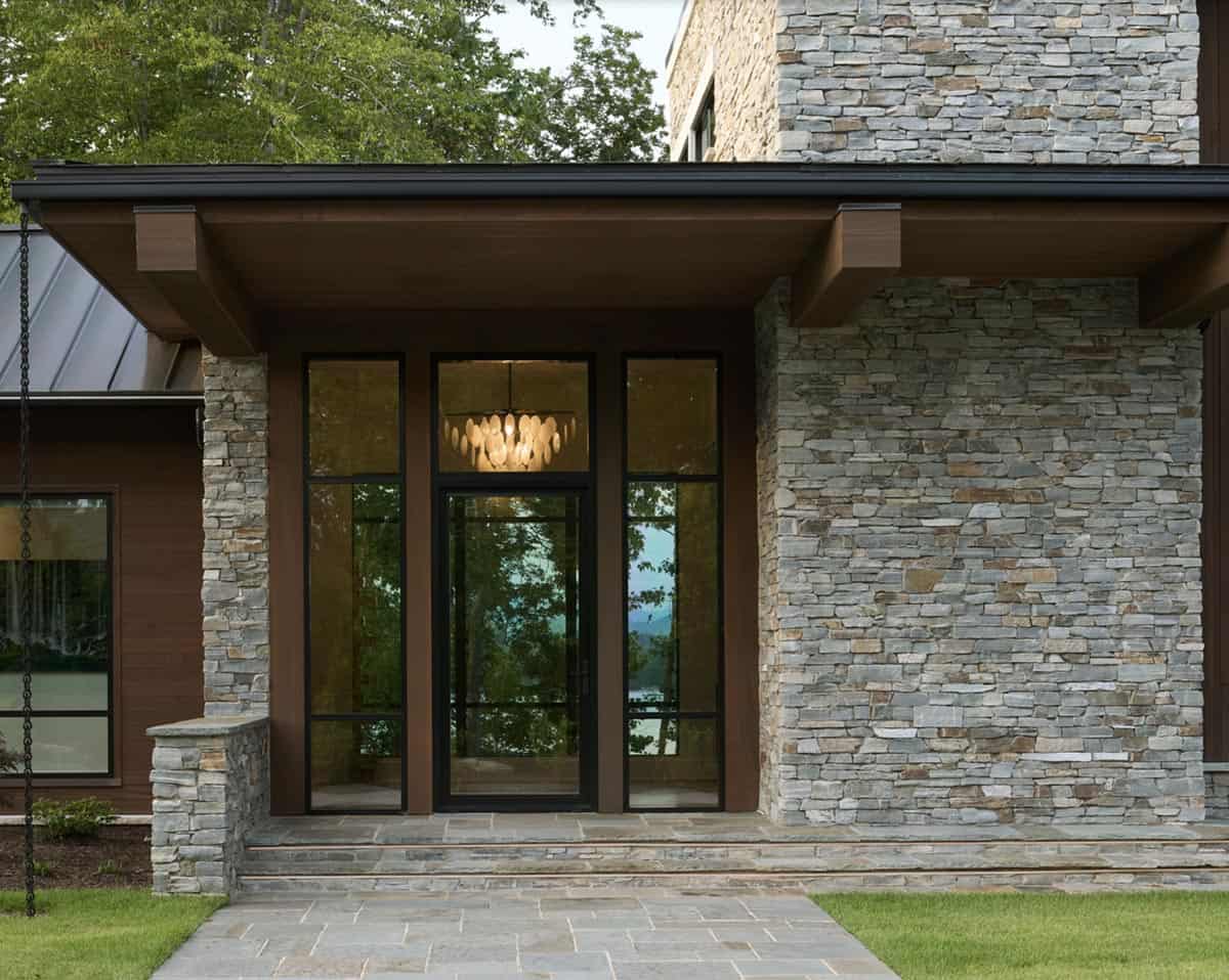 Front entrance with stacked stone columns, glass door, and lake view through the entry hall