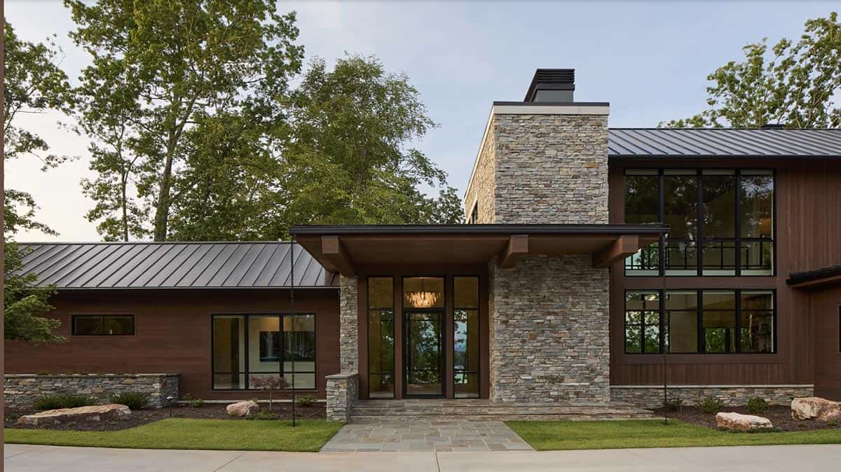 Front entry facade with stone chimney tower, glass door, and covered porch at dusk