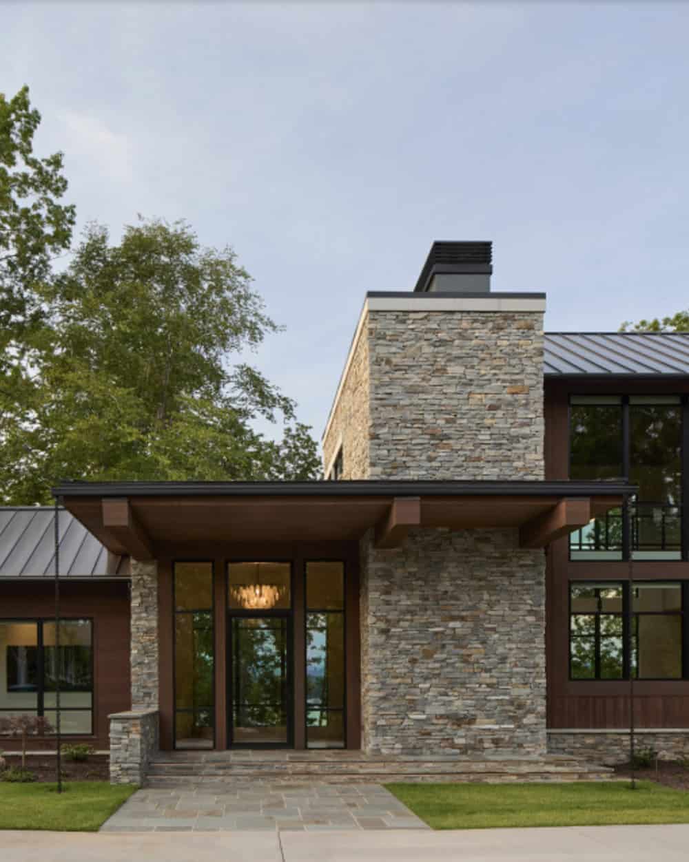 Front entry tower with stone cladding, glass doors, and chandelier glowing at dusk