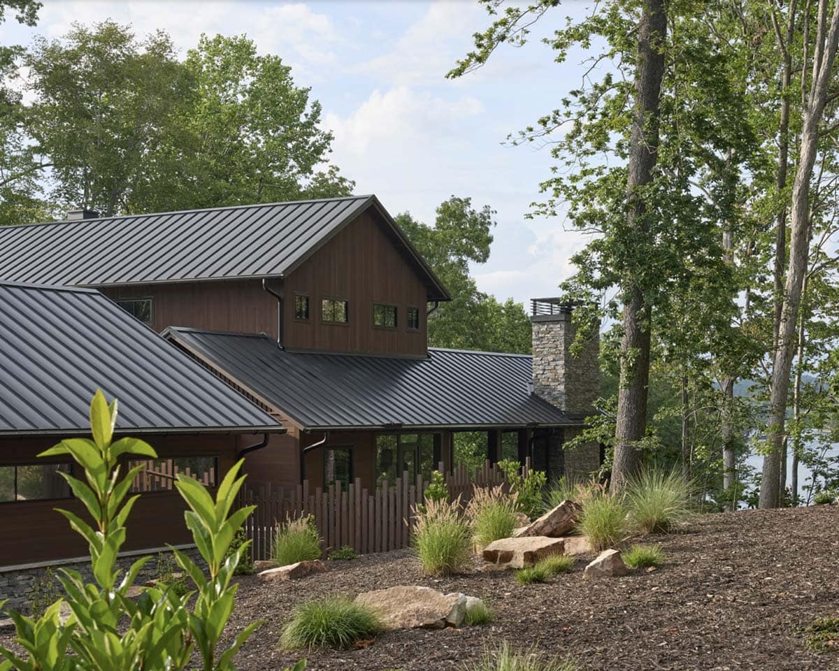 Rear exterior view of the wood-sided upper gable, stone chimney, and metal roof near the lake