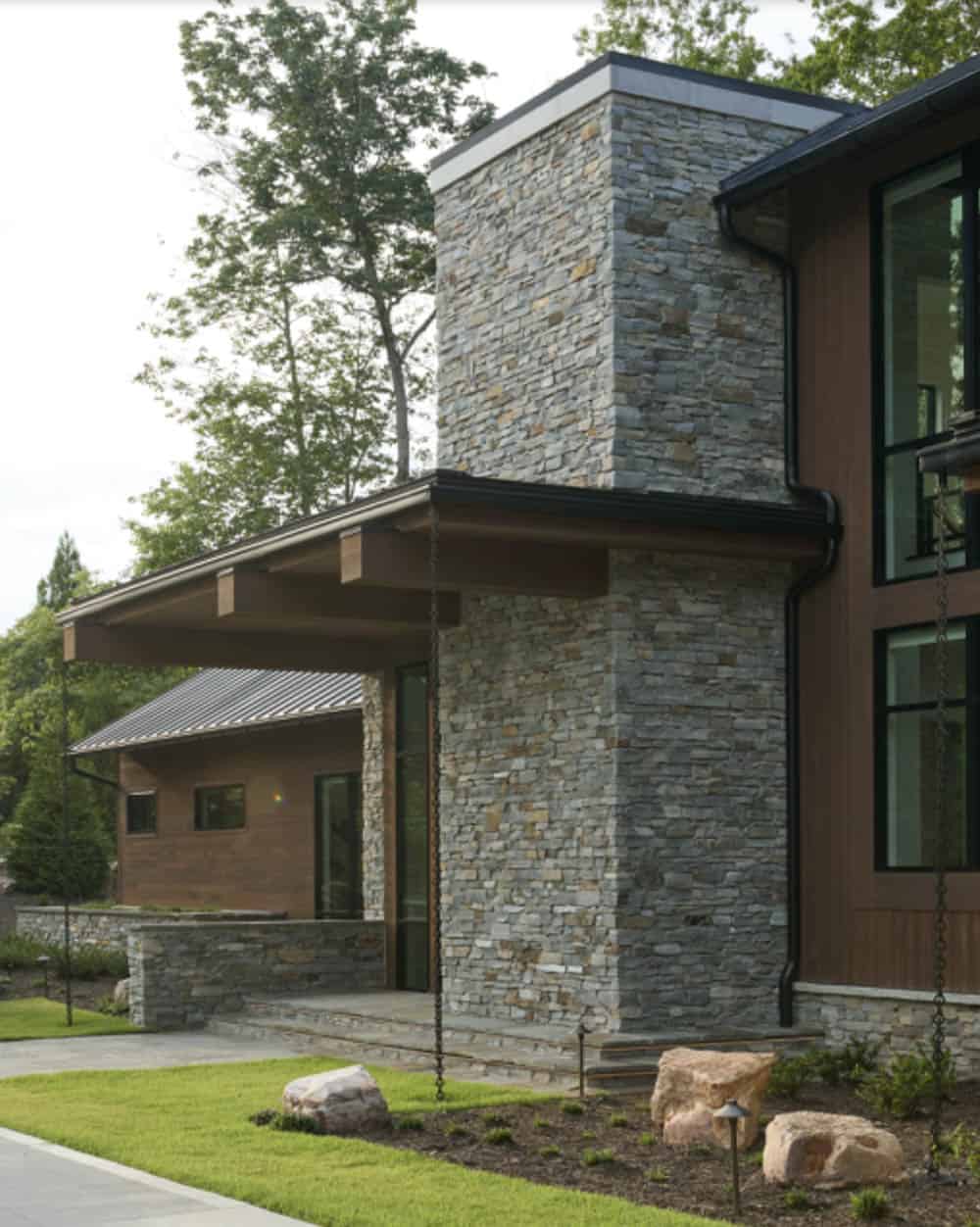 Close-up of the stacked stone entry tower with wood beam roof overhang and landscape lighting