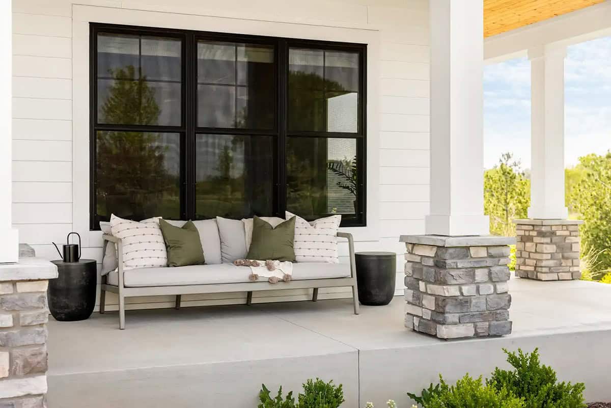 Outdoor sofa with green pillows on covered porch with stone column