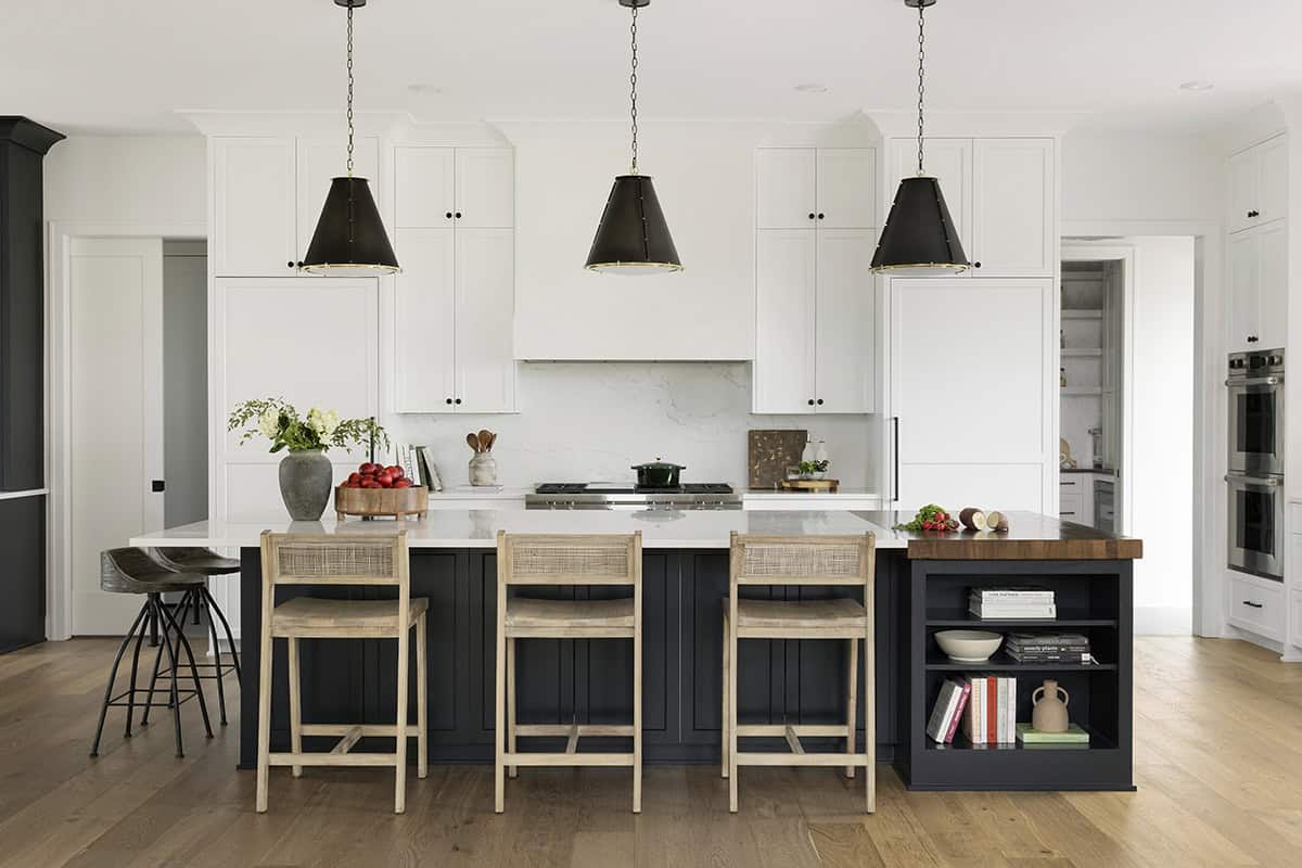 White kitchen with black island, cone pendant lights, and marble backsplash