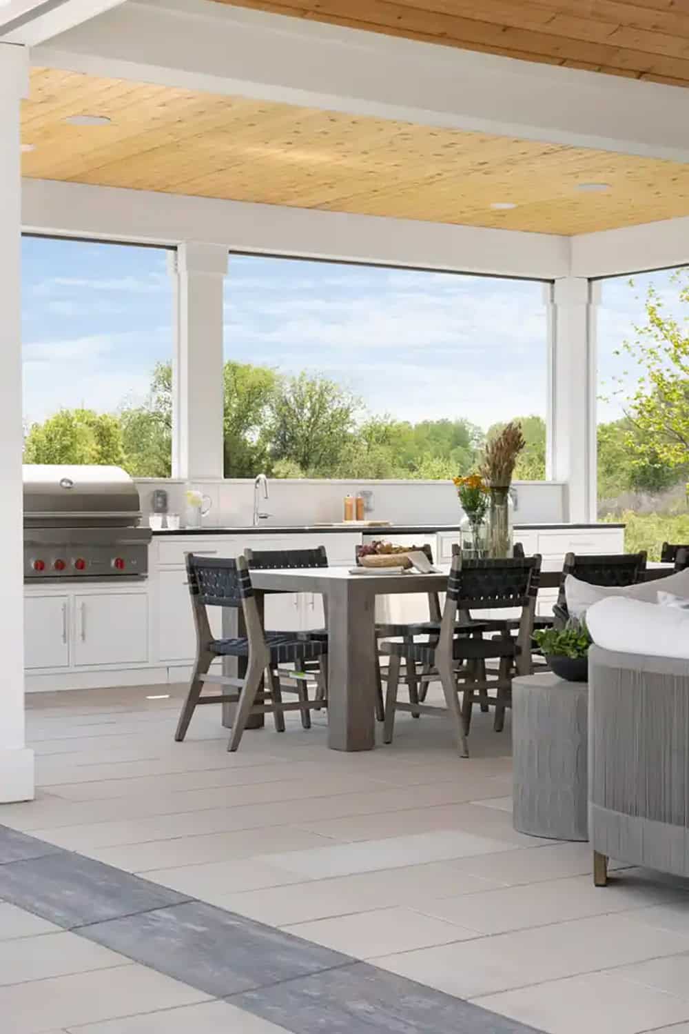 Outdoor kitchen and dining area under wood-paneled patio ceiling