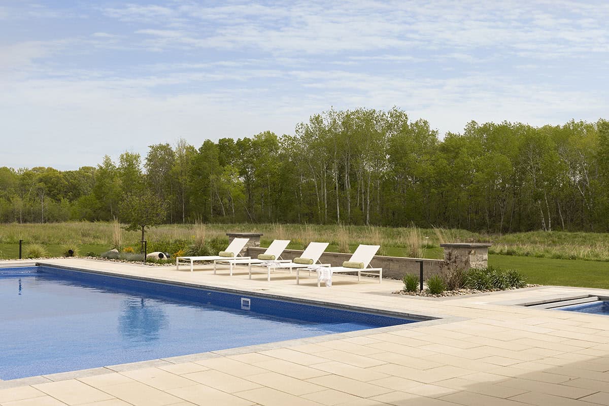 Rectangular pool with white lounge chairs and tree-lined backyard