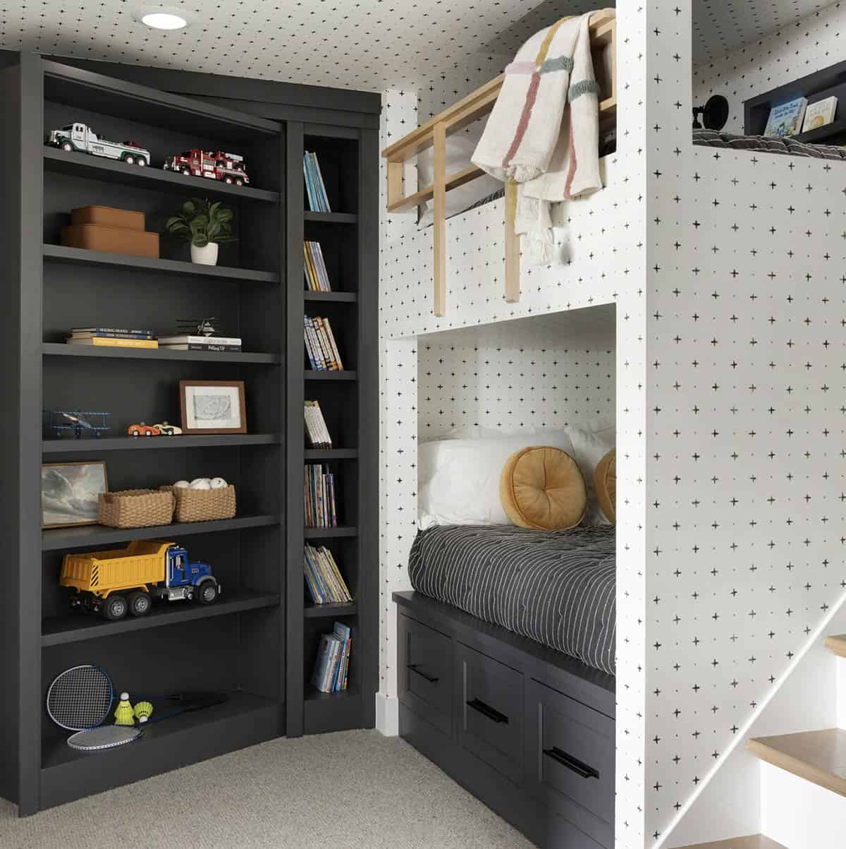 Bunk room built-in bookshelf with toys and books beside patterned bunk bed nook