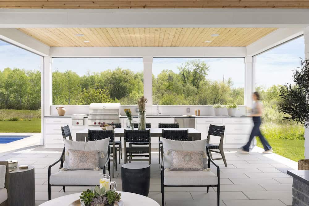 Covered outdoor living space with dining table, lounge chairs, and outdoor kitchen