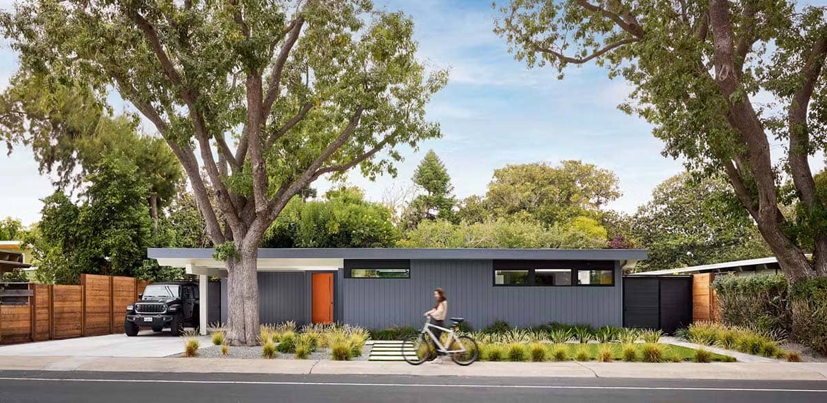 Gray Eichler exterior with orange door and mature street trees