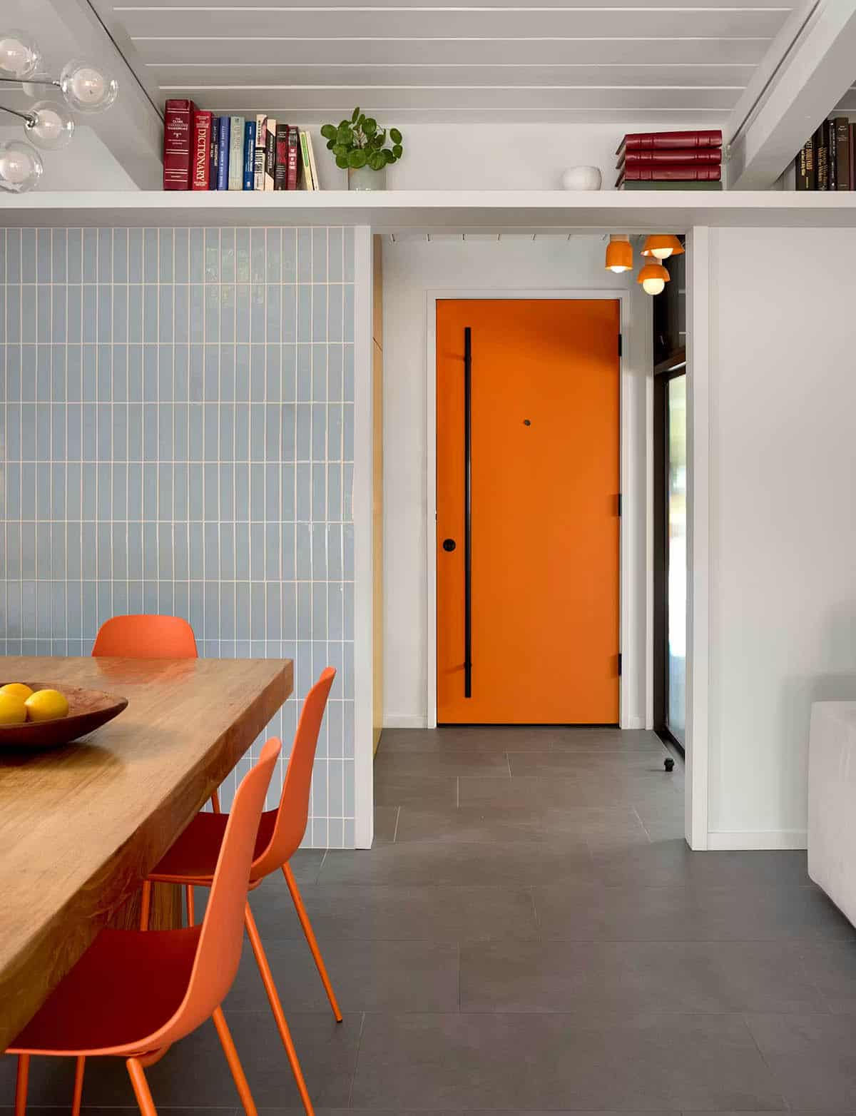 Orange door framed by blue tile wall and dining table