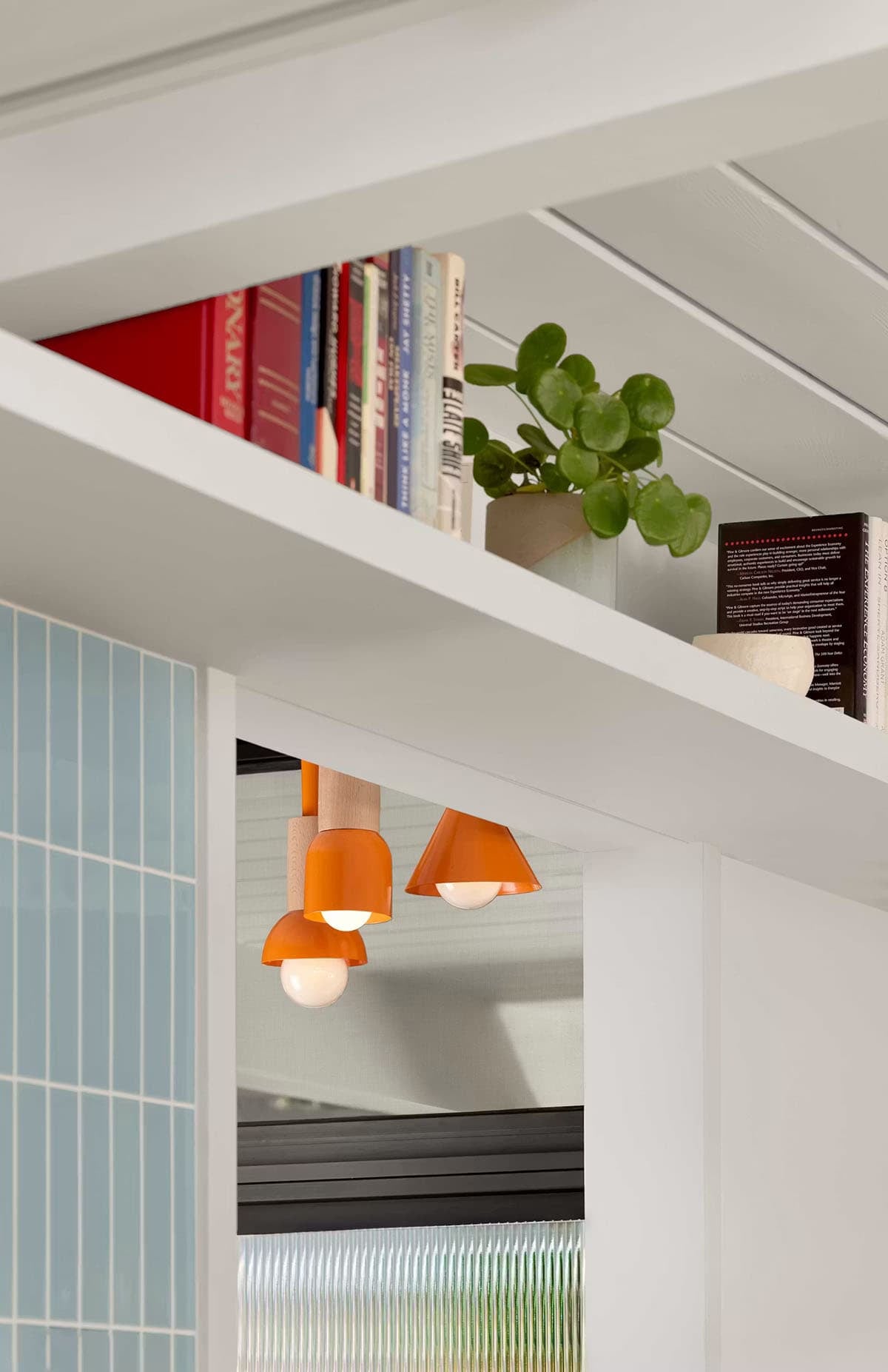 Orange pendant lights beneath open shelf with books and plant