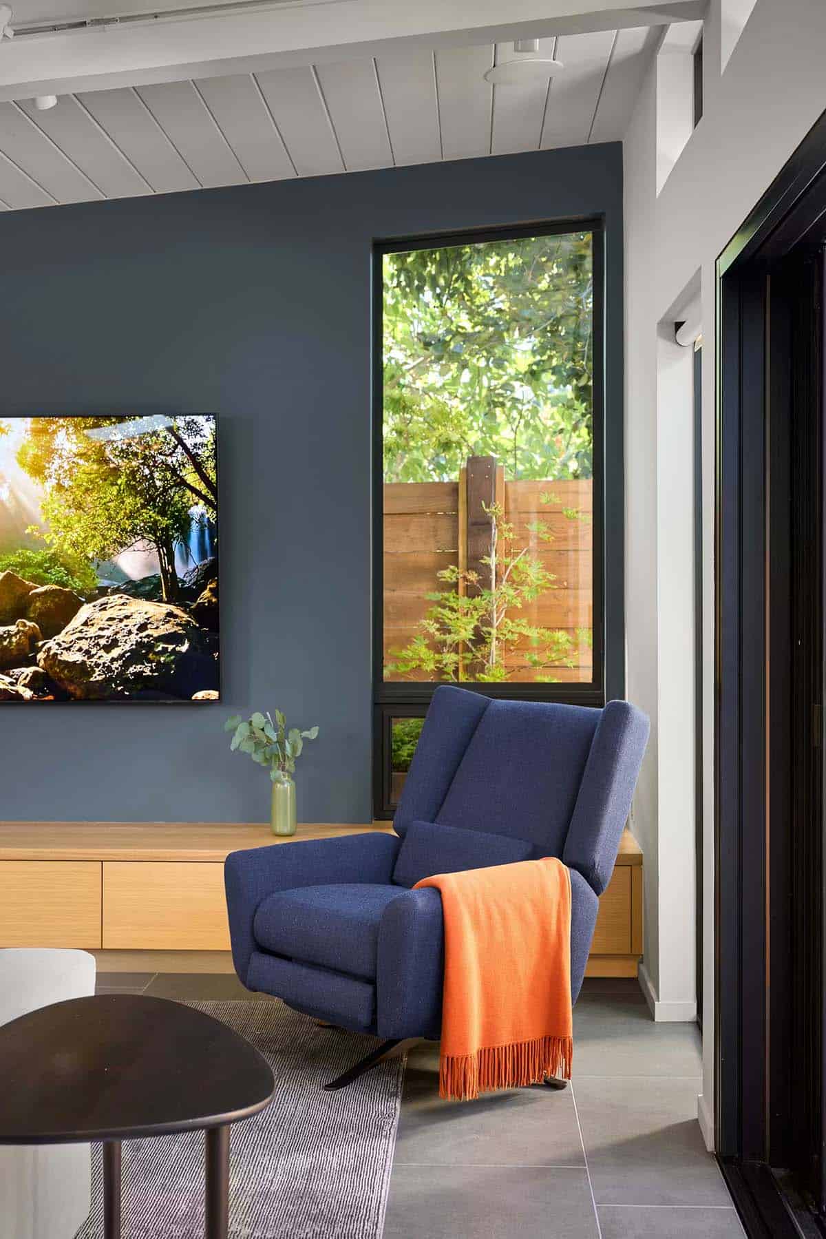 Navy blue recliner chair beside black accent wall and window