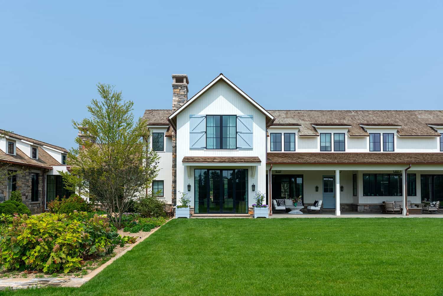 Rear exterior with covered porch and stone chimney overlooking lawn