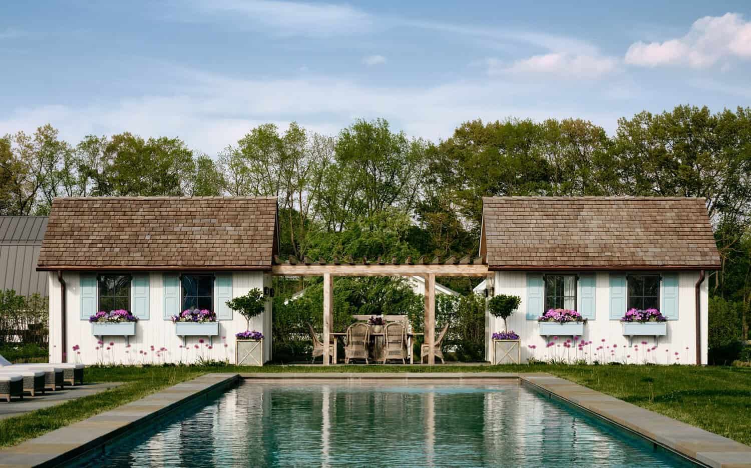 Pool flanked by matching pool houses with blue shutters and pergola