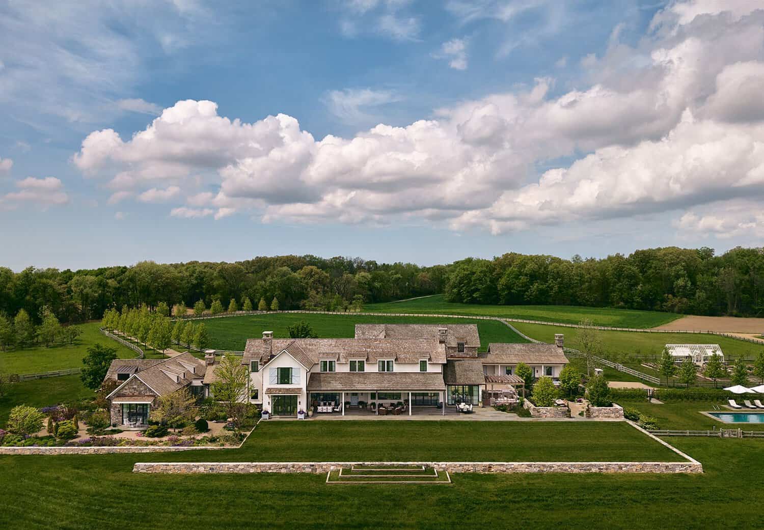 Aerial view of farmhouse estate with pool, greenhouse, and rolling fields
