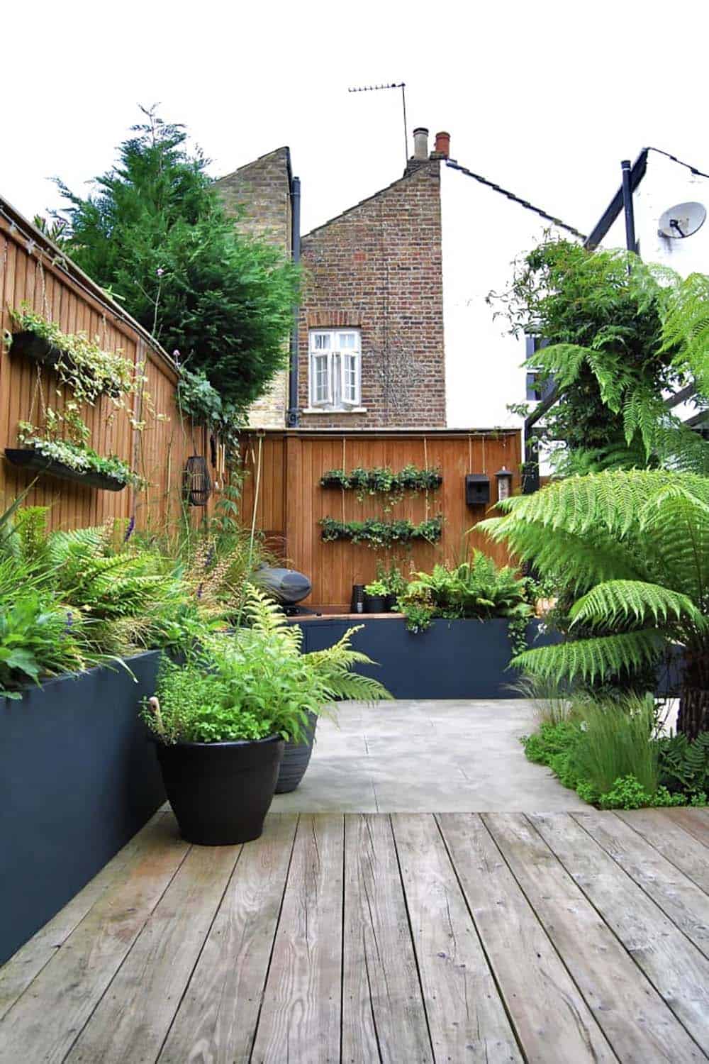 Wooden fence lined with hanging planters and lush ferns above a garden patio