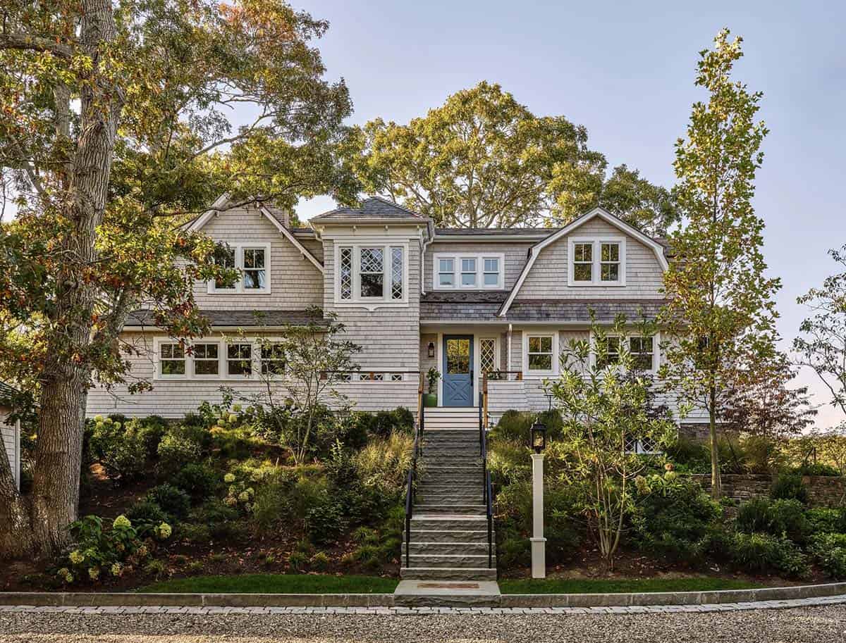 Shingle-style Cape Cod home exterior with blue front door, gambrel roof, and stone entry steps surrounded by trees