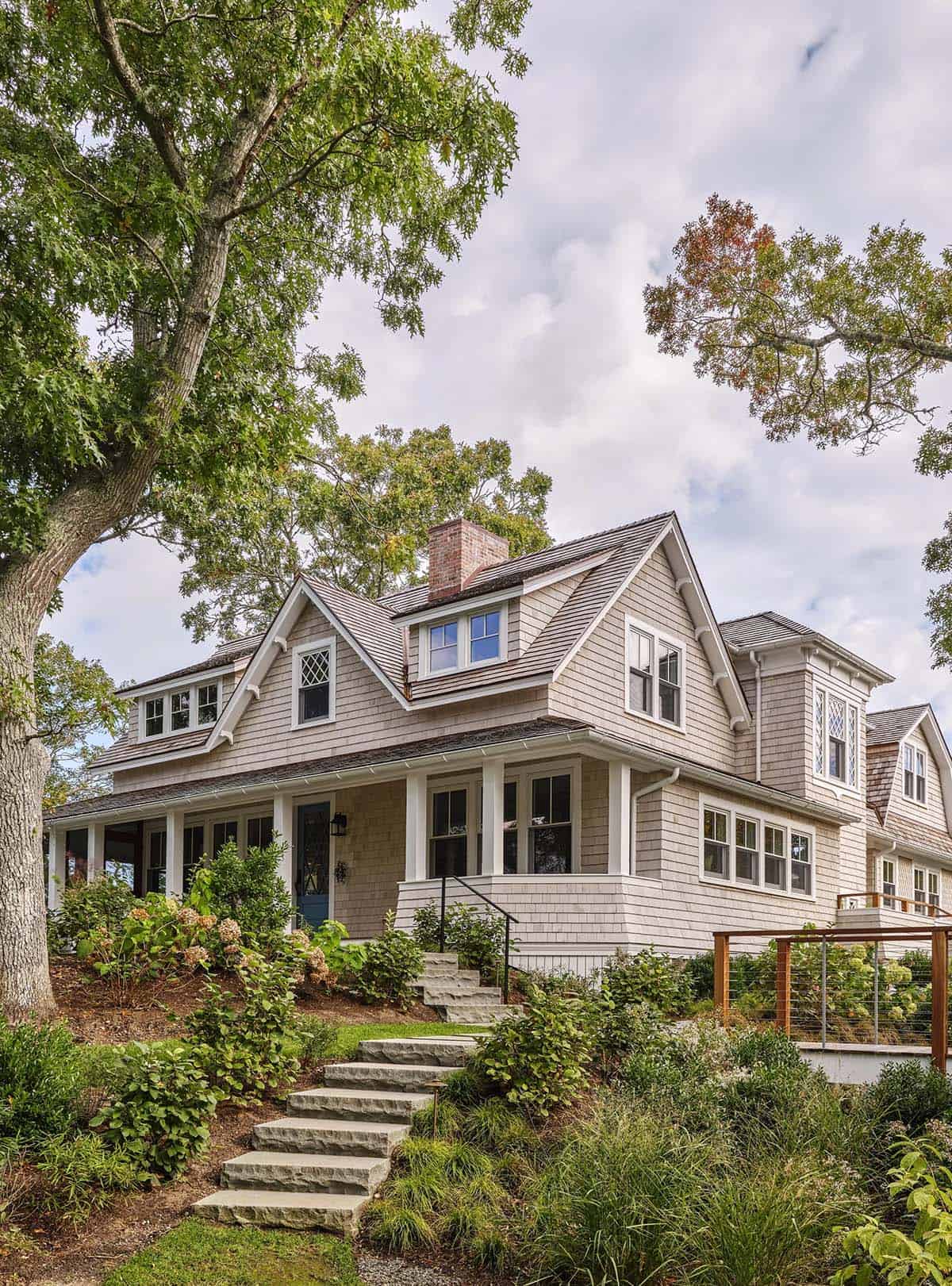 Side view of shingled cottage with dormers, wraparound porch, and stone garden steps