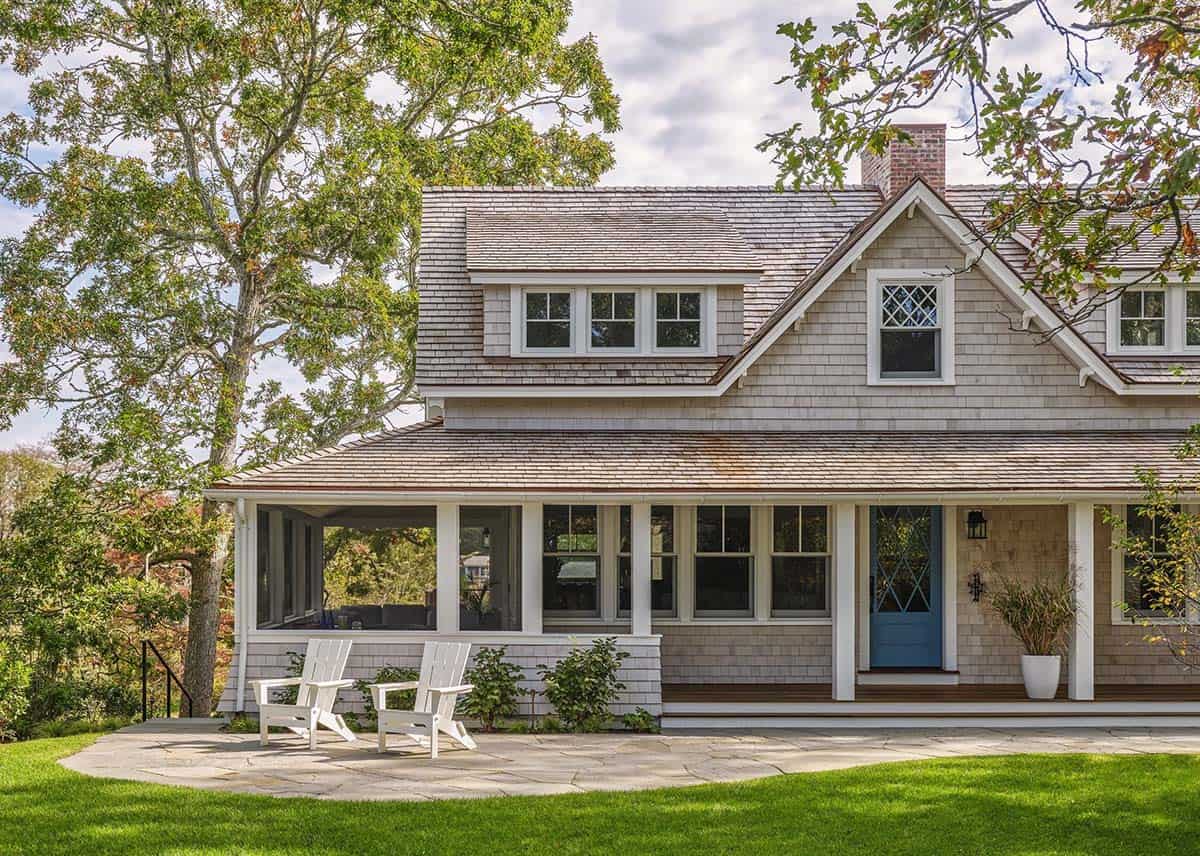 Wraparound porch with white columns, blue front door, and two white Adirondack chairs on a stone patio