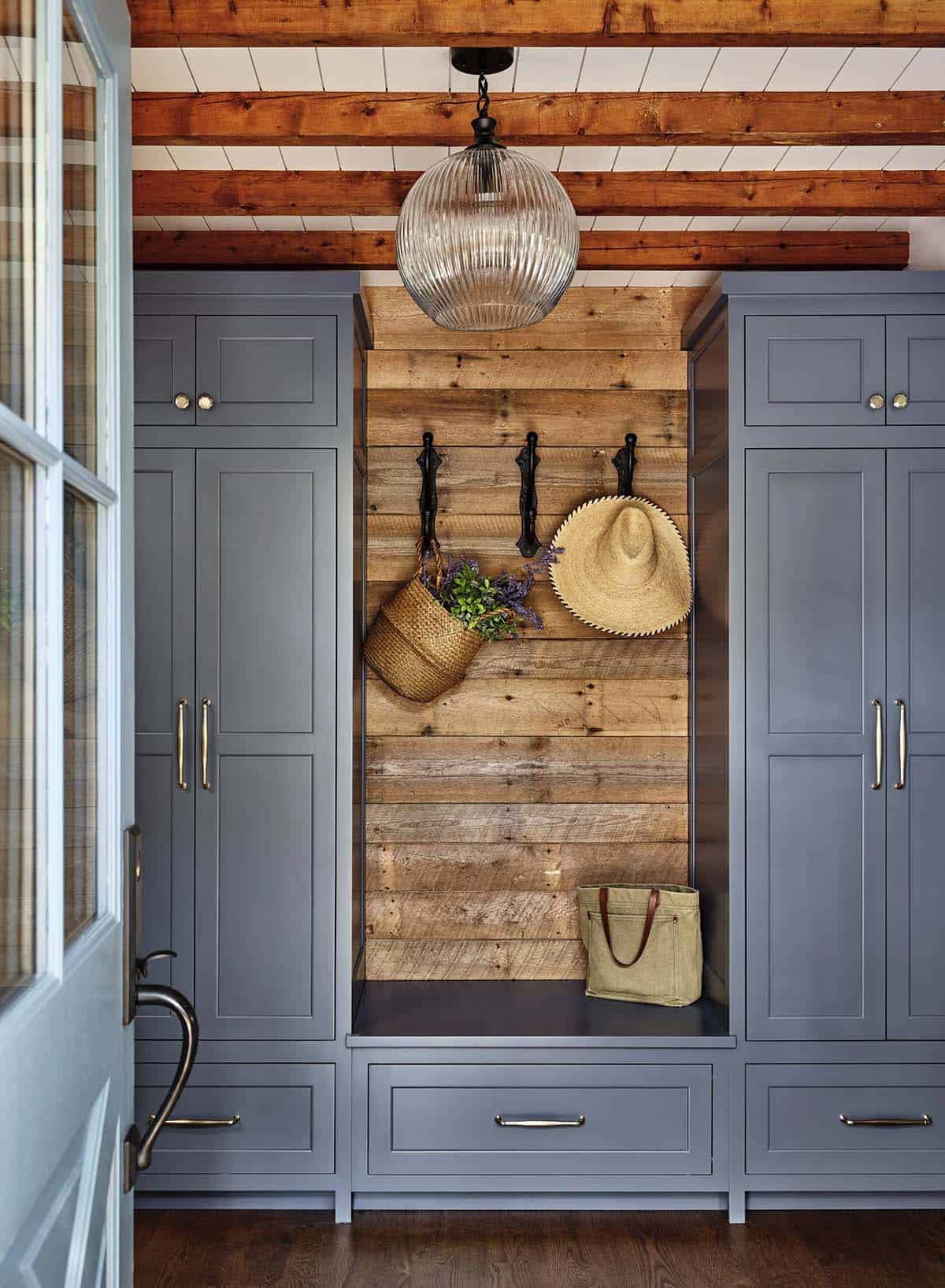 Mudroom nook with reclaimed wood paneling, black hooks, straw hat, and blue built-in cabinetry
