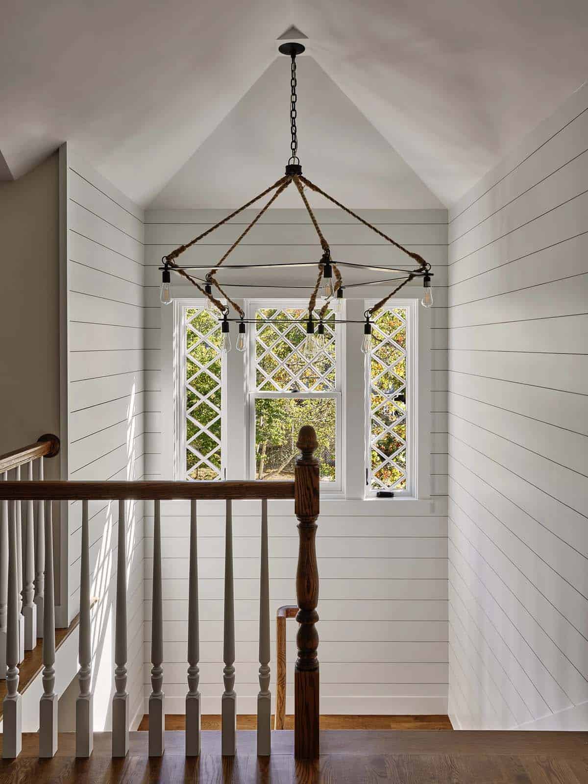 Stairwell landing with diamond-lattice window and rope-and-iron chandelier with exposed bulbs