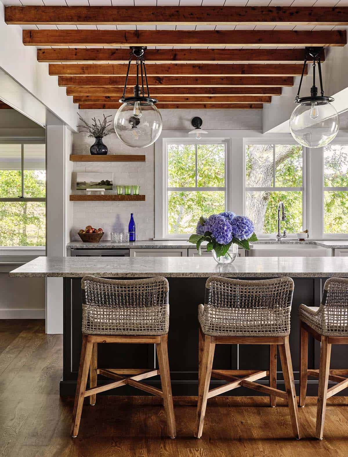Kitchen view toward window with hydrangea centerpiece, wood beams, and white subway tile backsplash