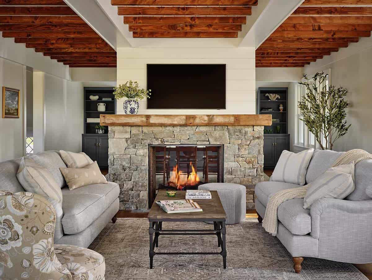 Living room with stone fireplace, wood mantel, gray sofas, and exposed ceiling beams