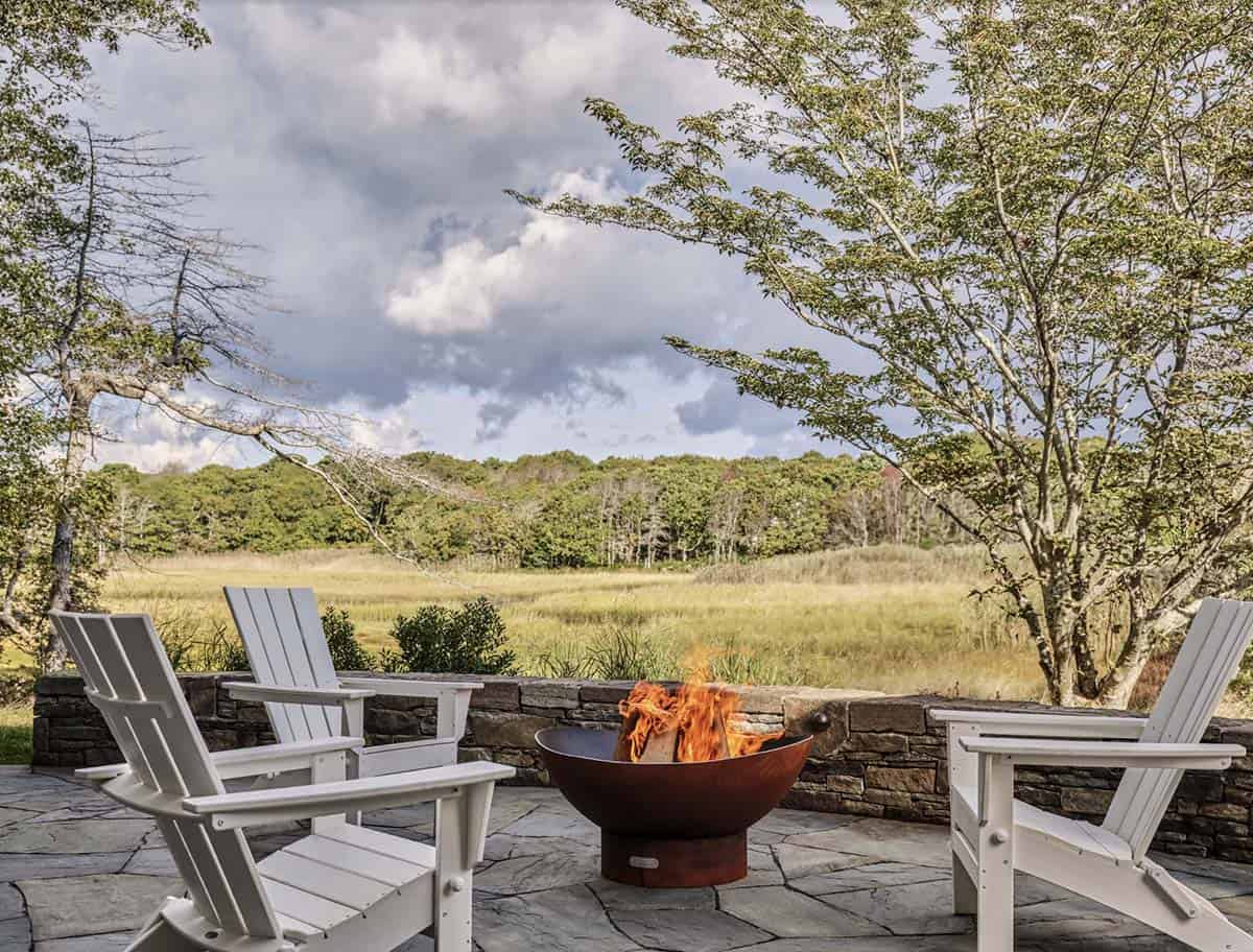 Stone patio with white Adirondack chairs around a fire pit overlooking a marsh landscape