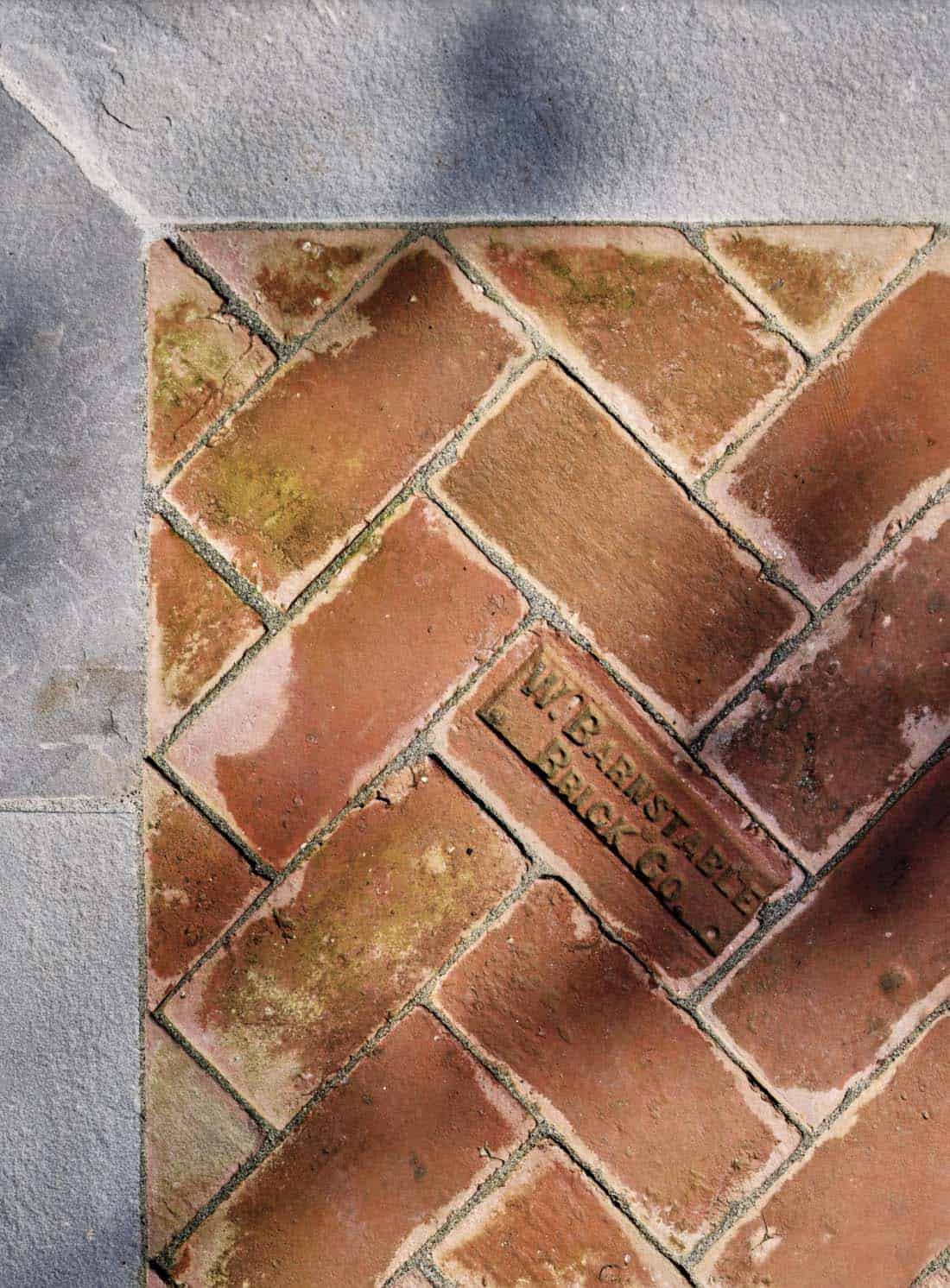 Close-up of herringbone brick pavers stamped "W. Barnstable Brick Co." bordered by bluestone
