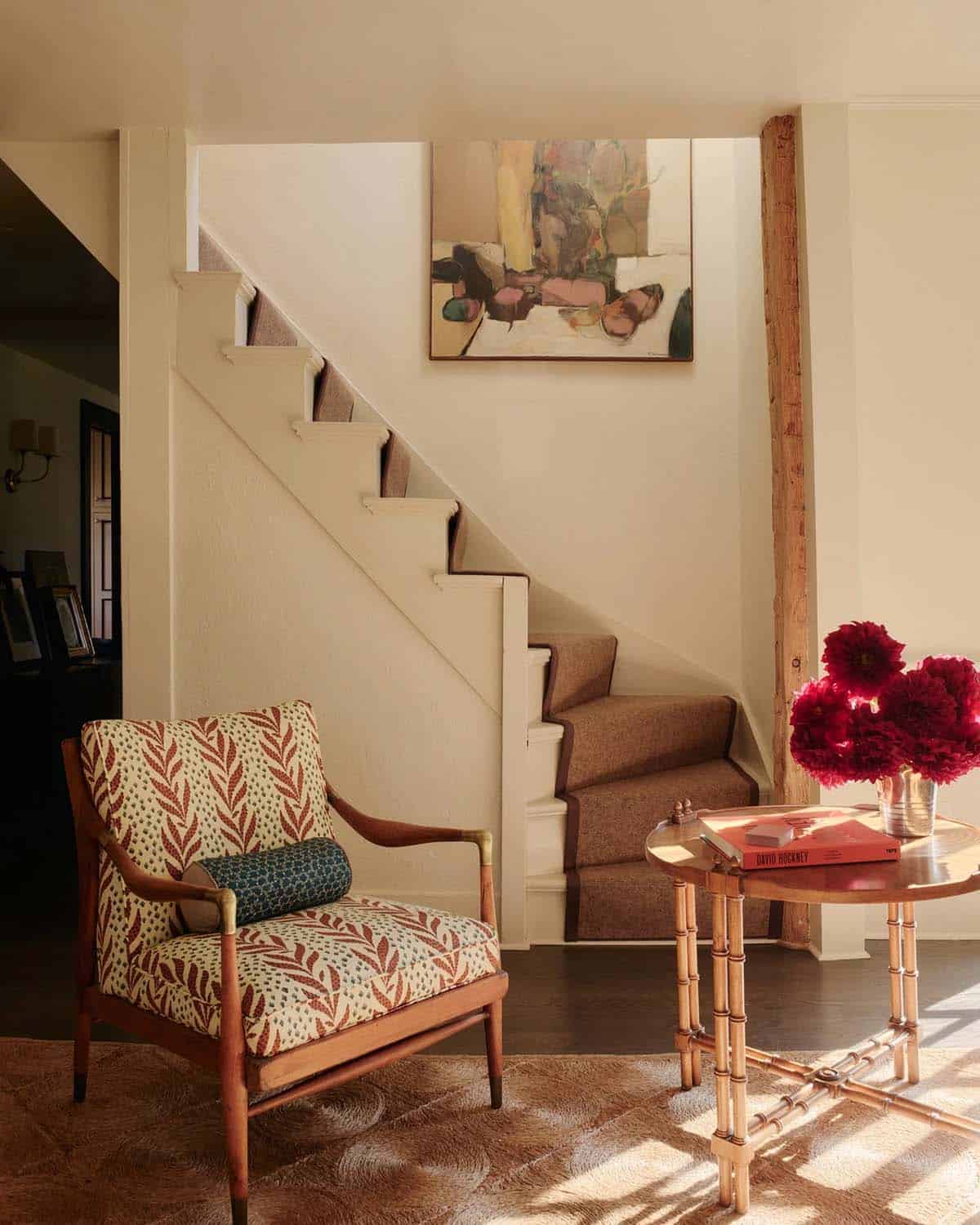 Staircase with brown carpet runner, patterned armchair, and abstract painting on landing