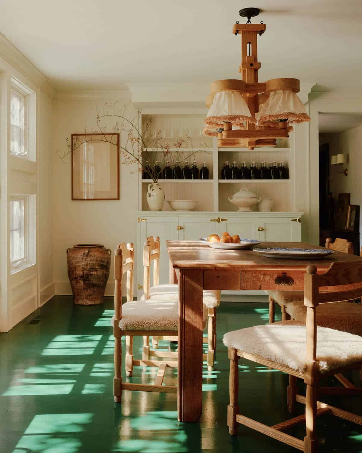 Dining room with green painted floor, rustic wood table, and sheepskin-seated chairs