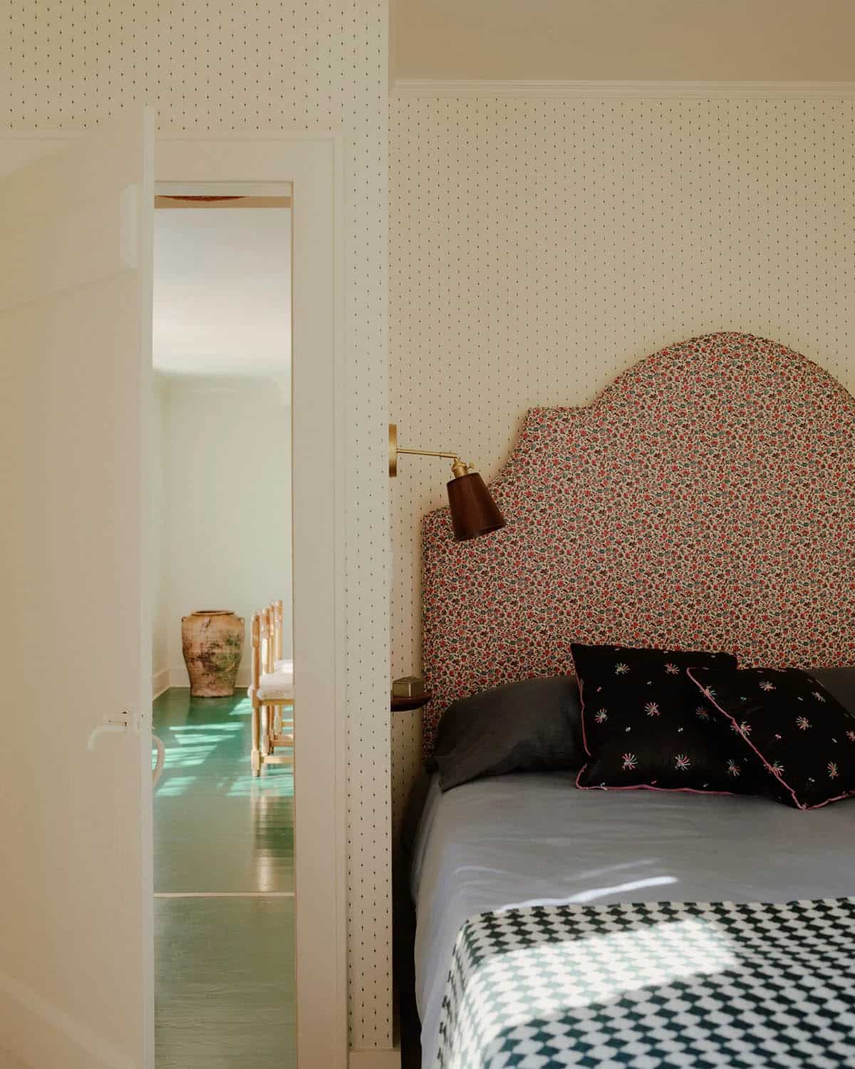 Bedroom with floral arched headboard, brass sconce, and dotted wallpaper