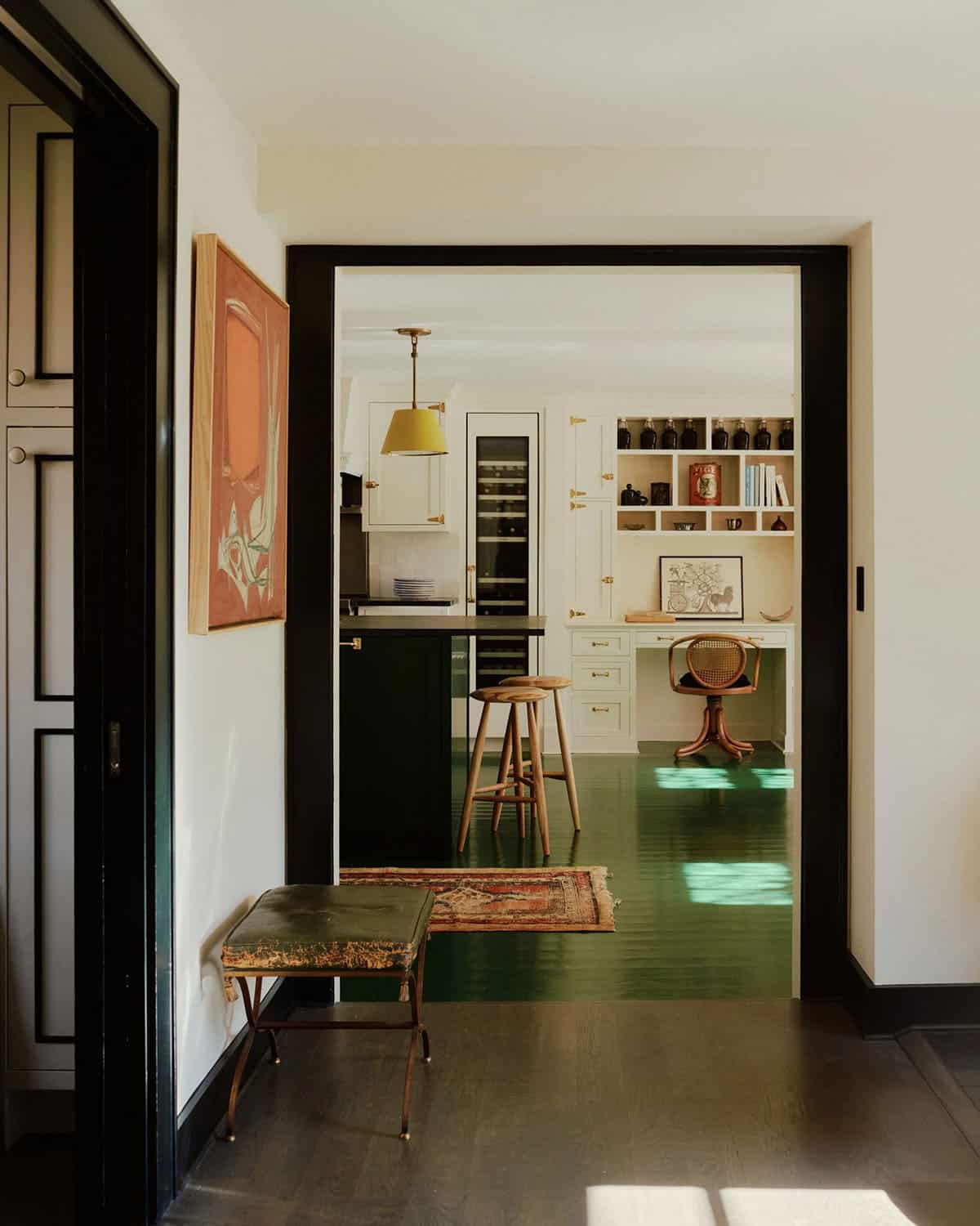 Hallway with black-trimmed doors leading into green-floored kitchen