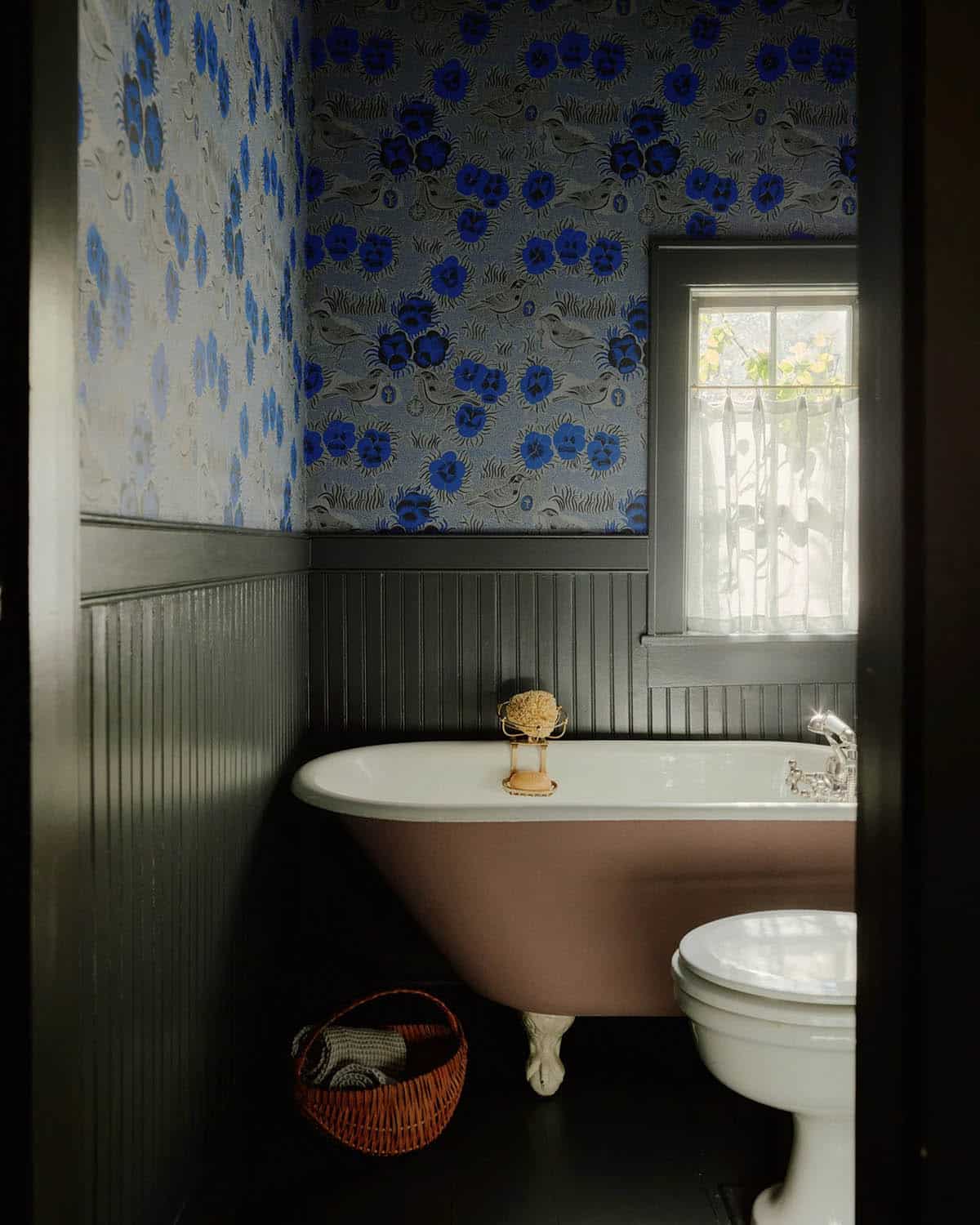Powder room with blue floral wallpaper, dark wainscoting, and pink clawfoot tub