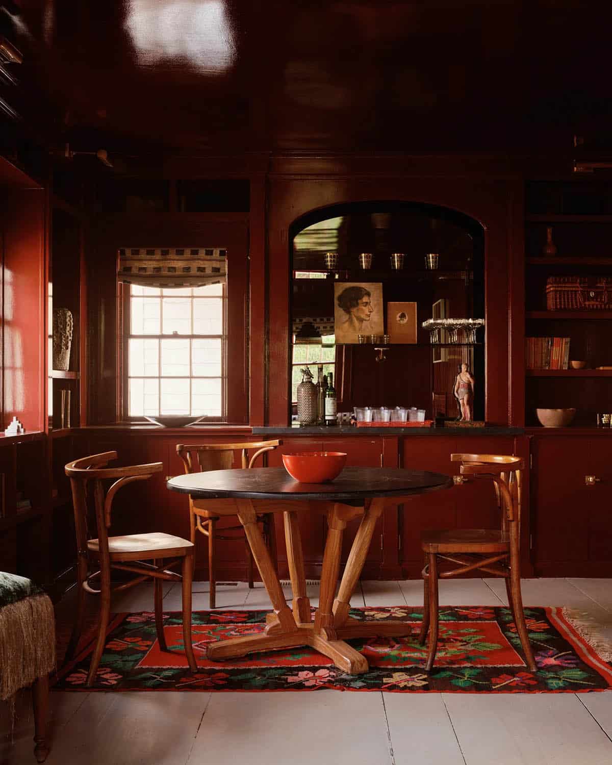 Red lacquered dining room with round table, bentwood chairs, and floral kilim rug