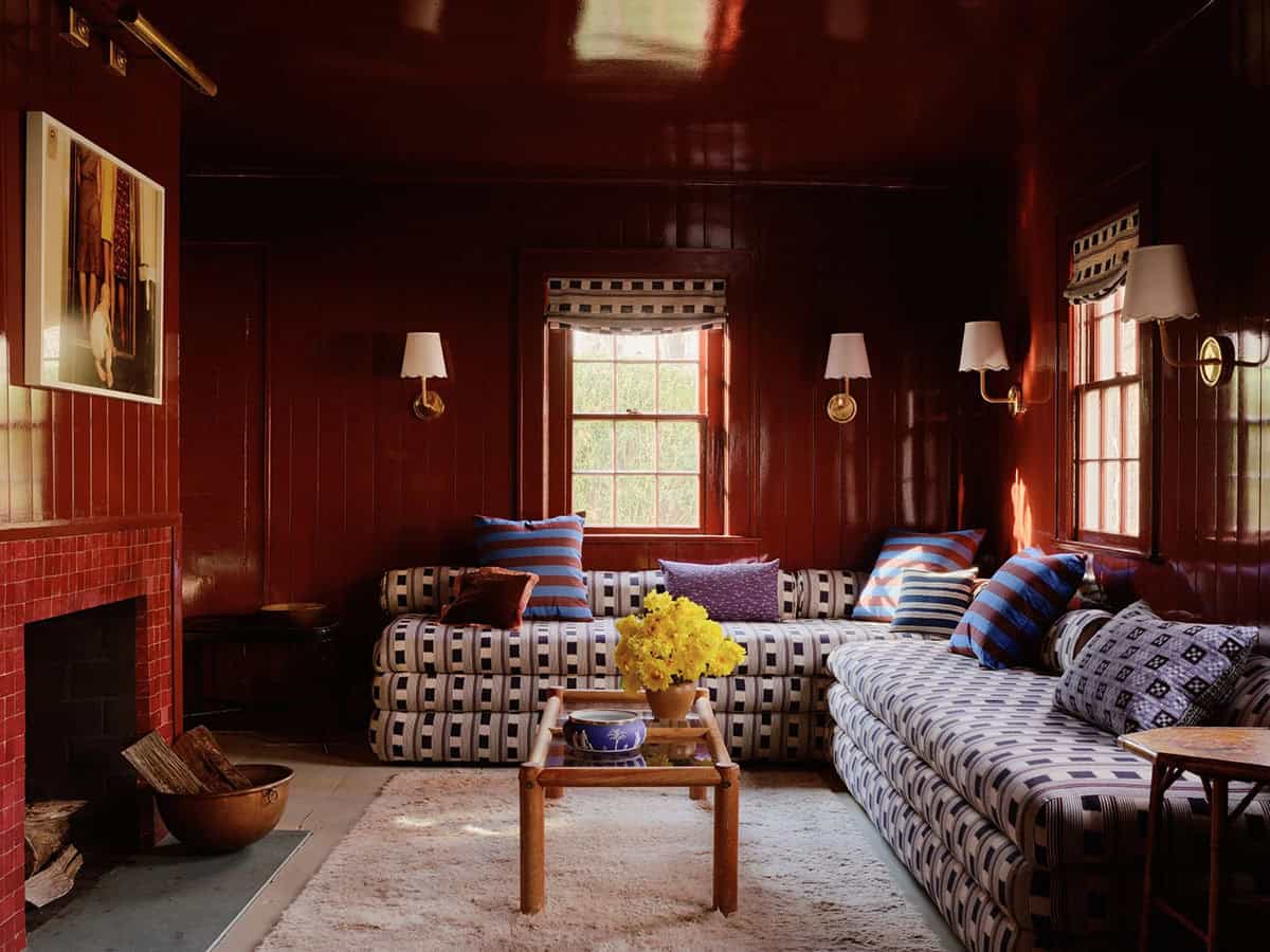 Red lacquered den with patterned sectional daybed seating and brass sconces