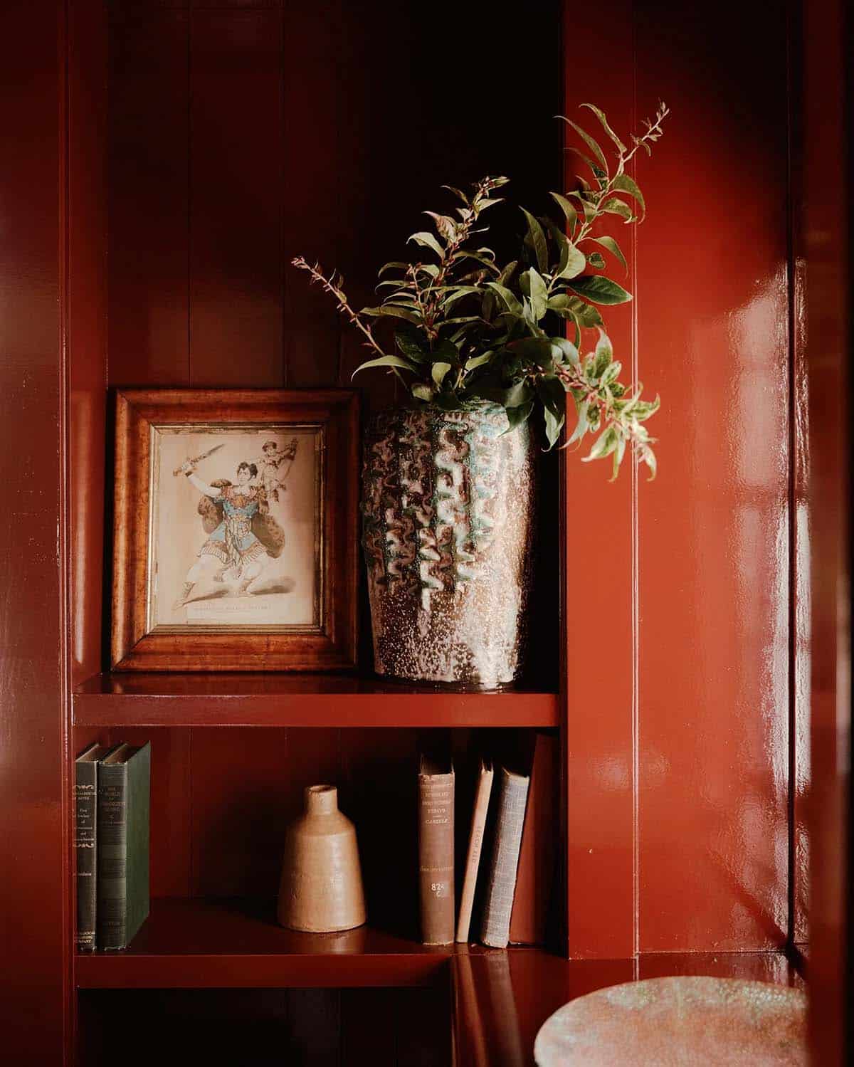 Red lacquered shelving with framed art, ceramic vase, and books