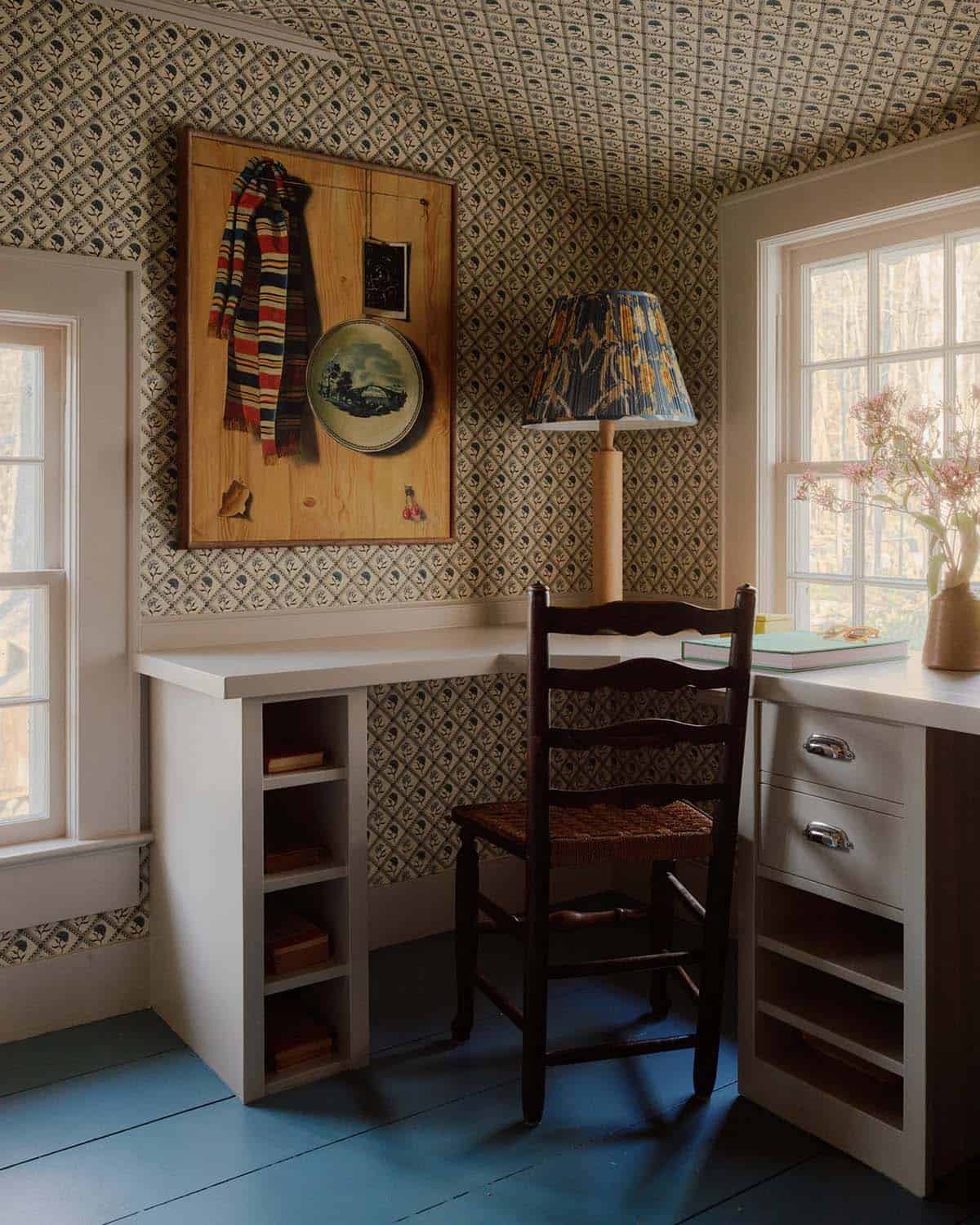 Desk nook with patterned wallpaper, ladder-back chair, and pleated lampshade