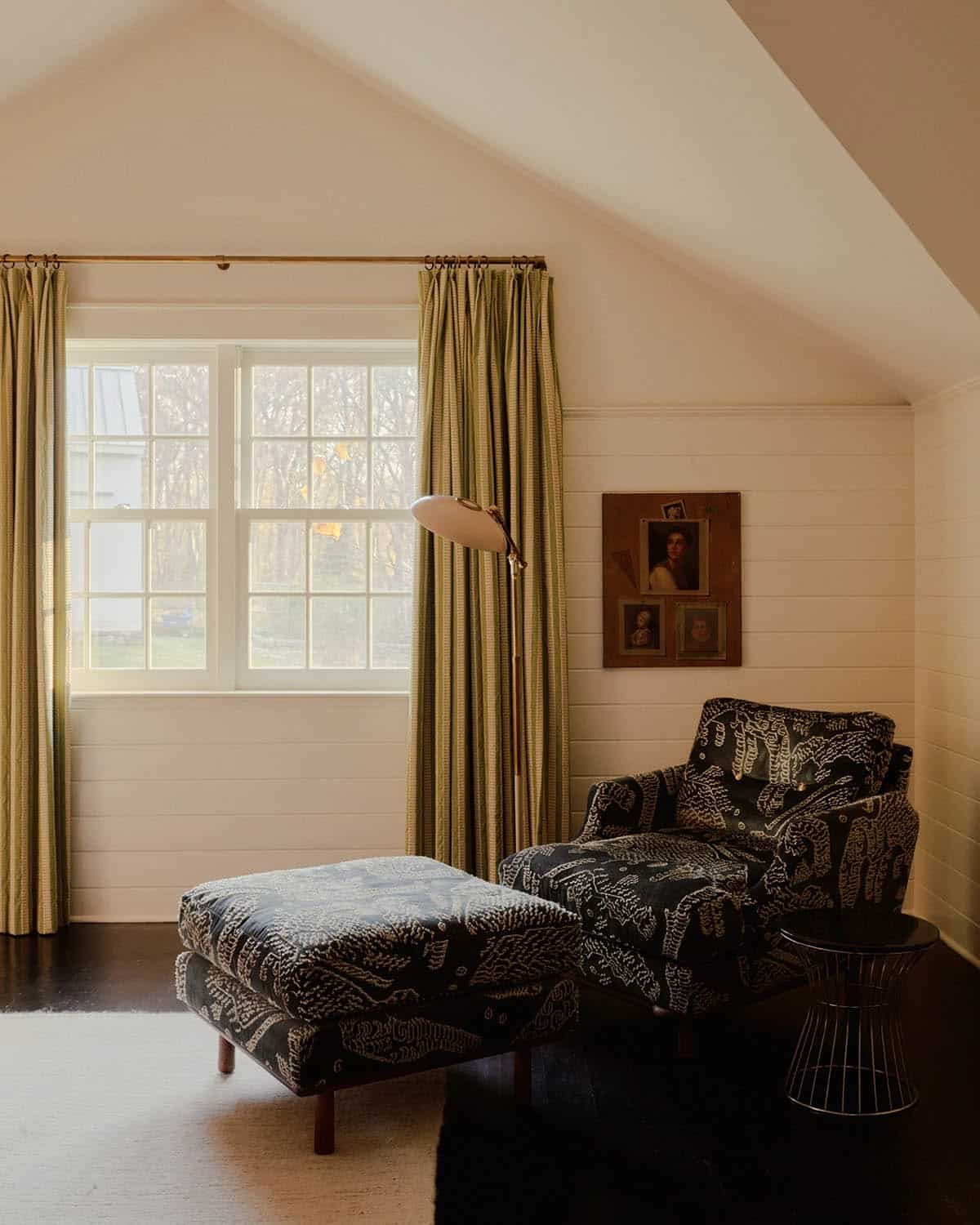 Attic sitting area with patterned chaise, ottoman, and floor lamp by dormer window